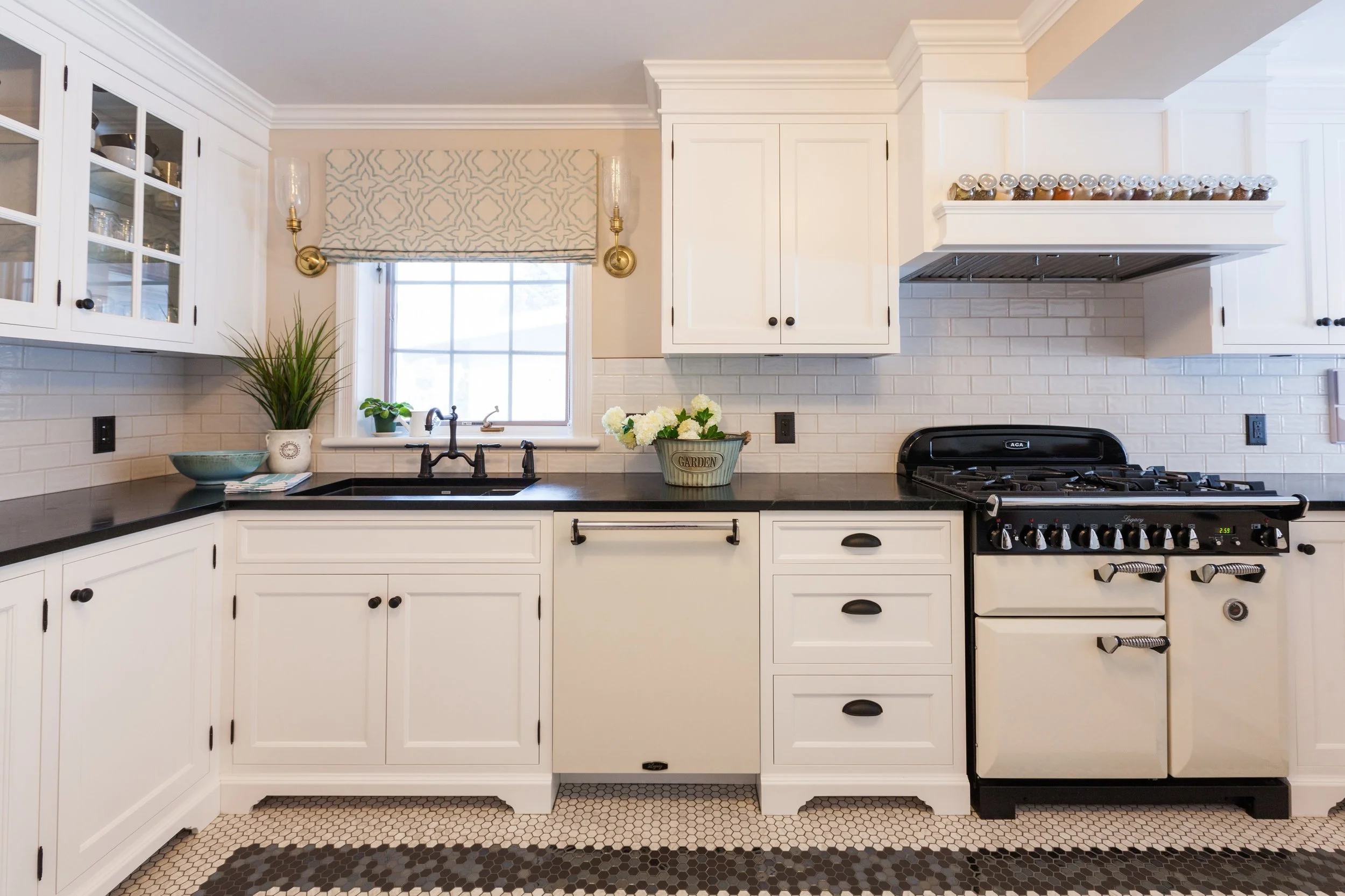 Kitchen with white cabinets, black countertop, gas stove, window with window treatment, potted plants, flowers, and hexagon tile floor.