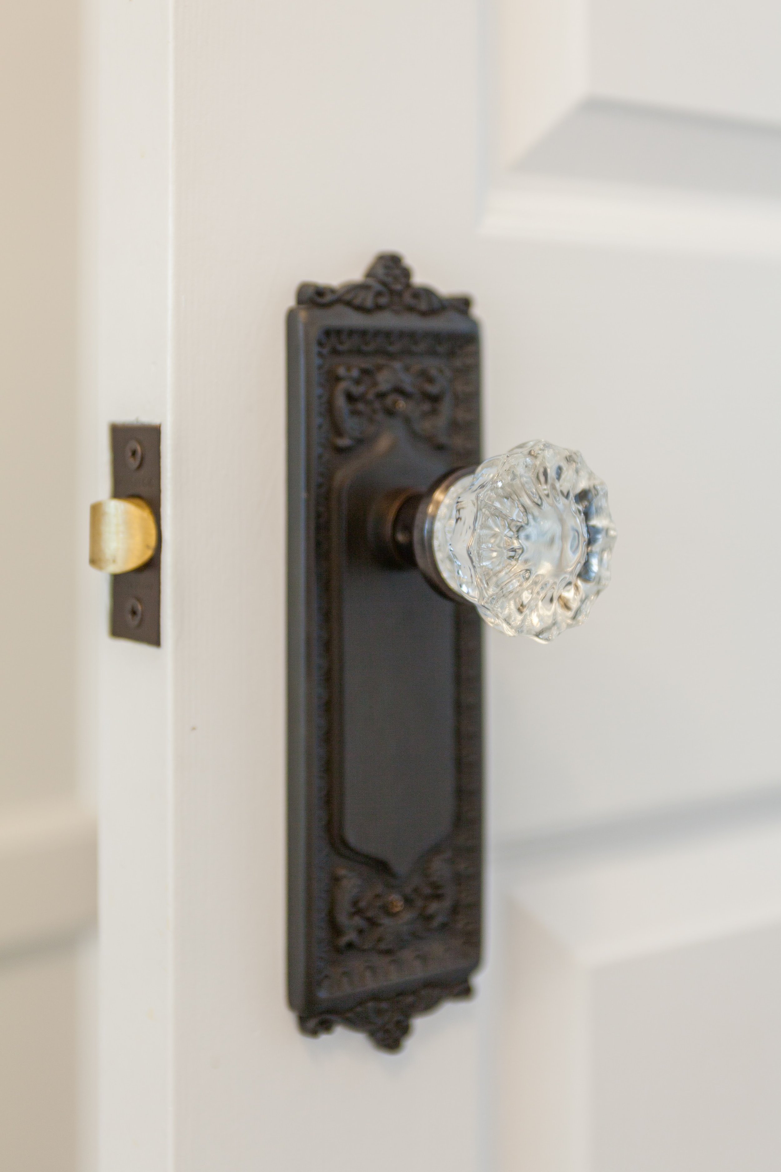 Close-up of a vintage door knob with an ornate backplate and clear glass handle on a white door.