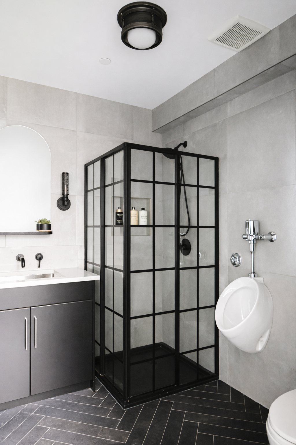 Modern bathroom with gray tiles, black framed glass shower enclosure, and a white urinal.