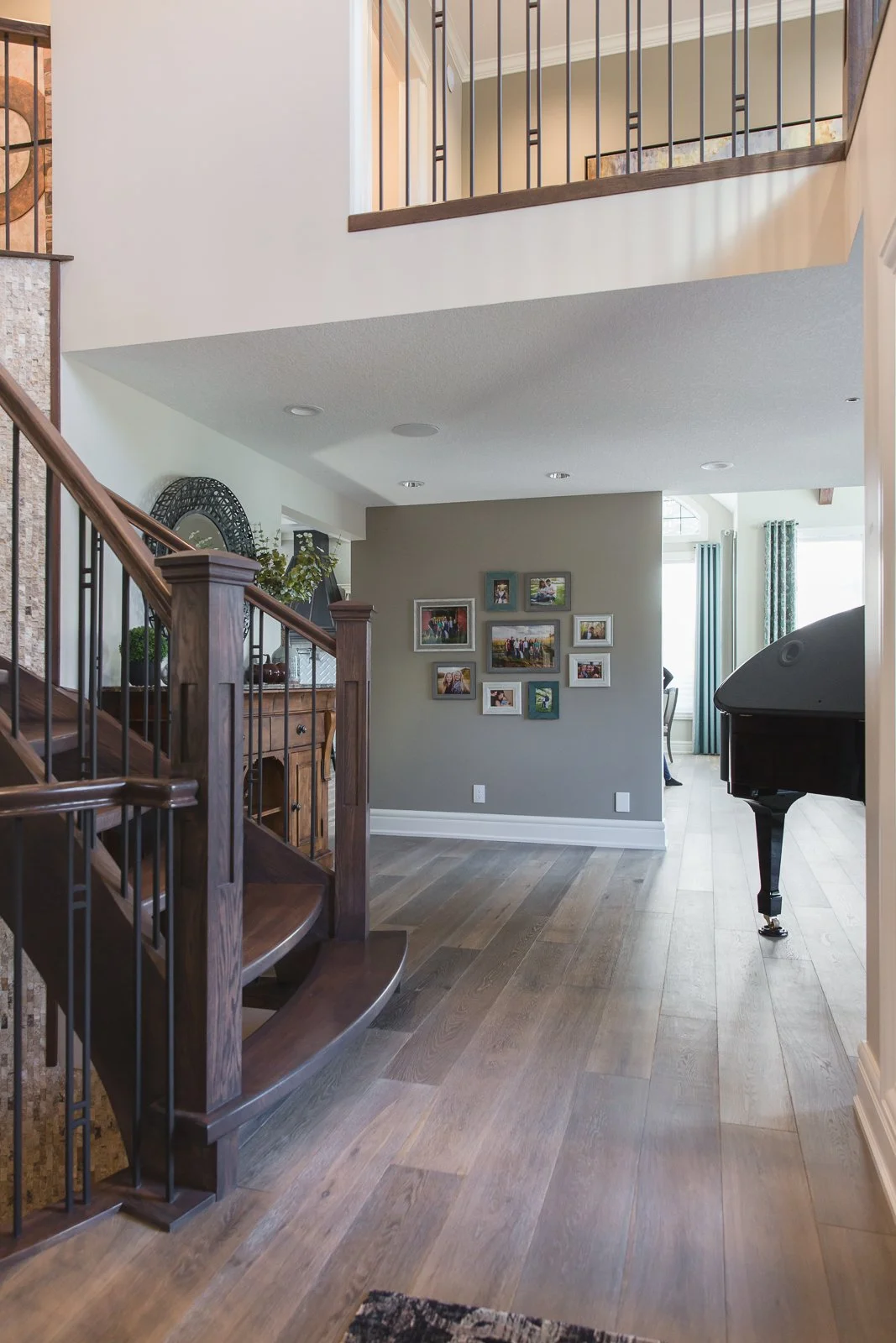 Interior view of a home with wooden stairs, a piano, a photo wall, and a dining area in the background.