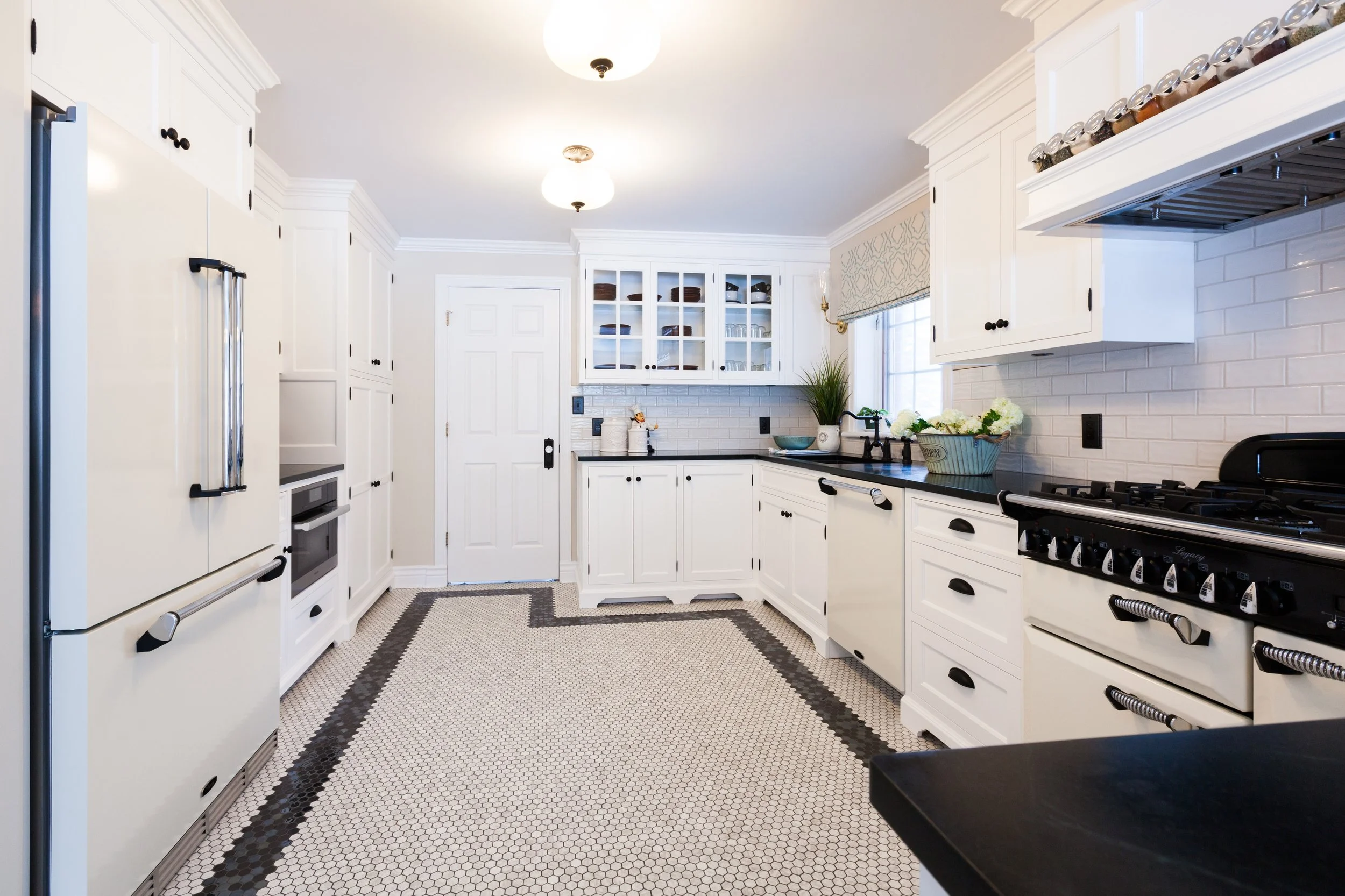 White kitchen with black countertops, hexagonal tile floor, and black cabinet handles.