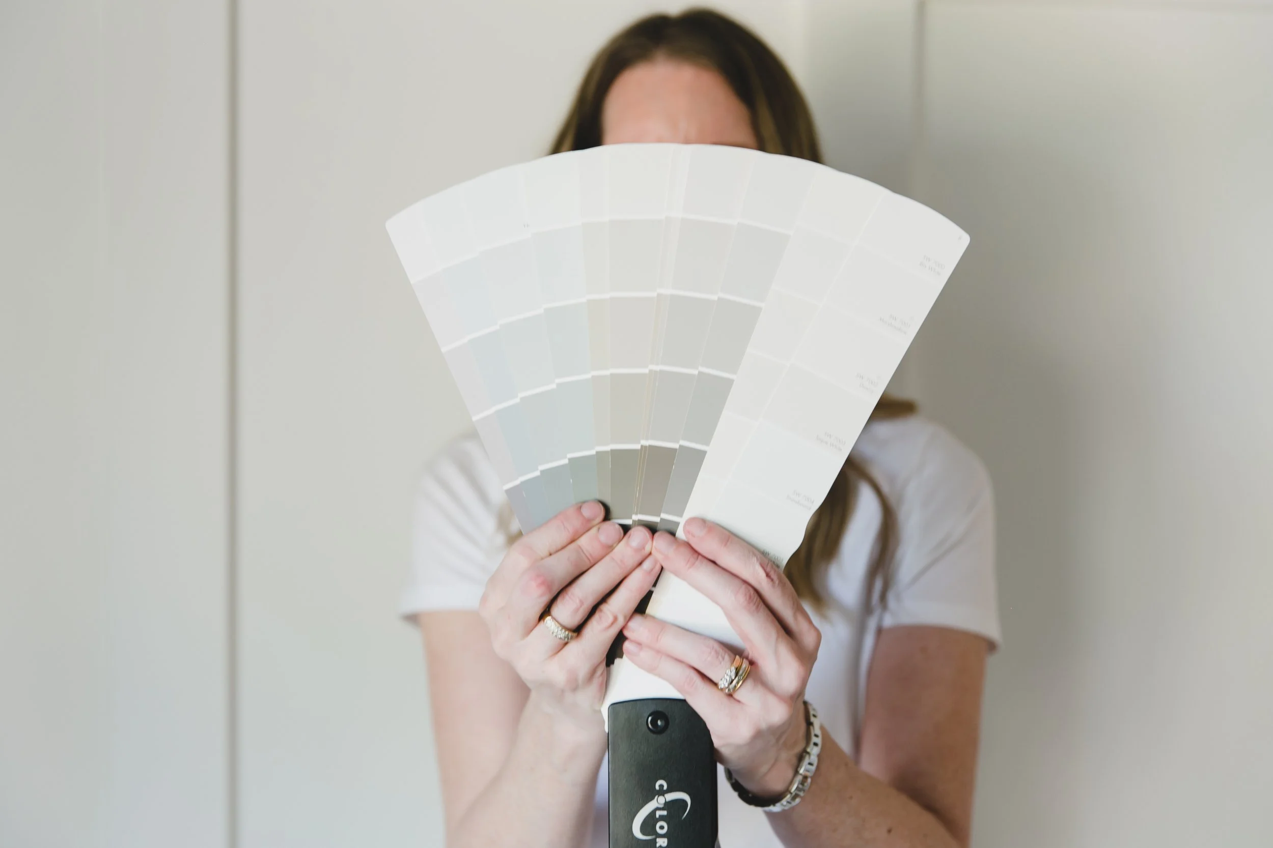Person holding a fan deck of color swatches in front of their face, showing various shades of gray and white.