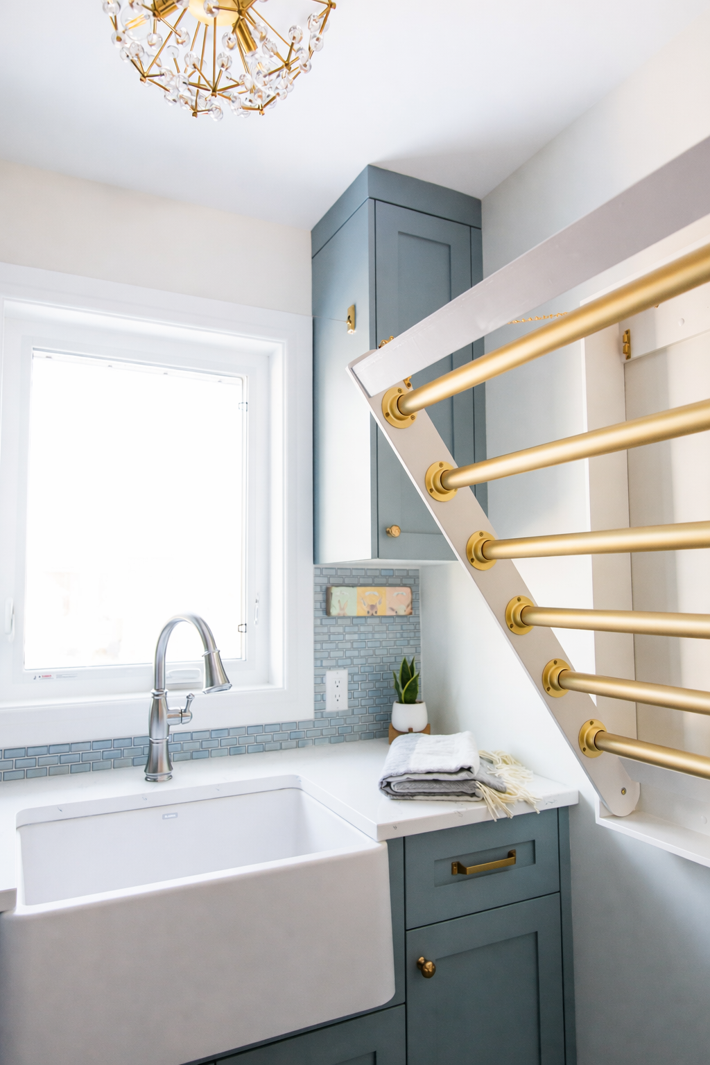 Close-up of a laundry or utility room with a sink, window, blue cabinetry, and a staircase with gold handrails.