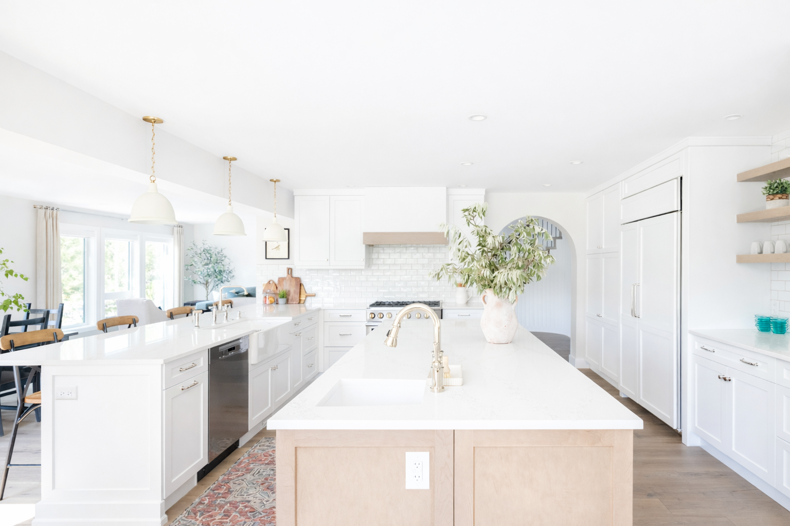 Bright white modern kitchen with island, large flowers in a white vase, and white cabinetry.