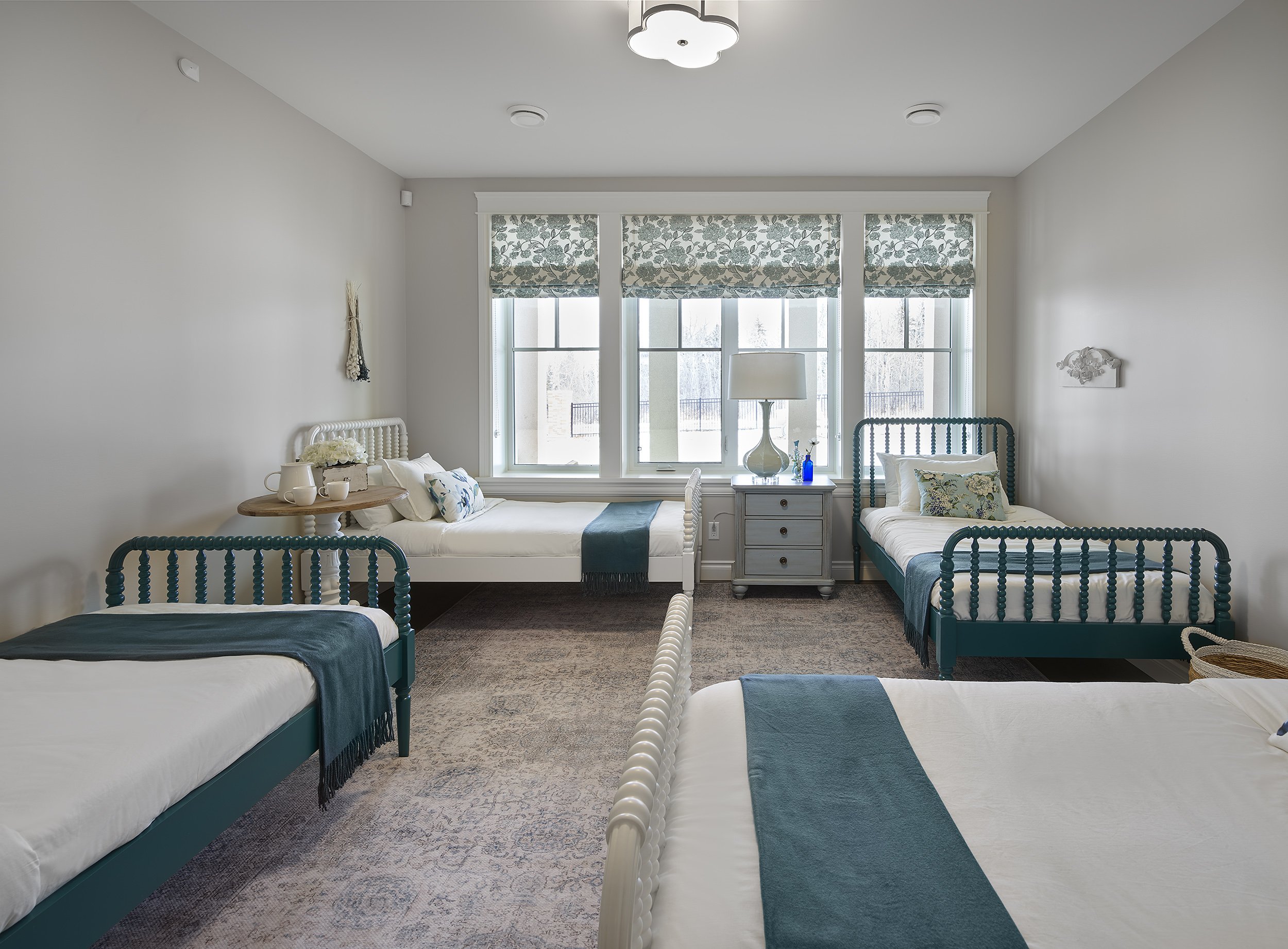 A bedroom with four beds, a gray nightstand, and a window with floral blinds.