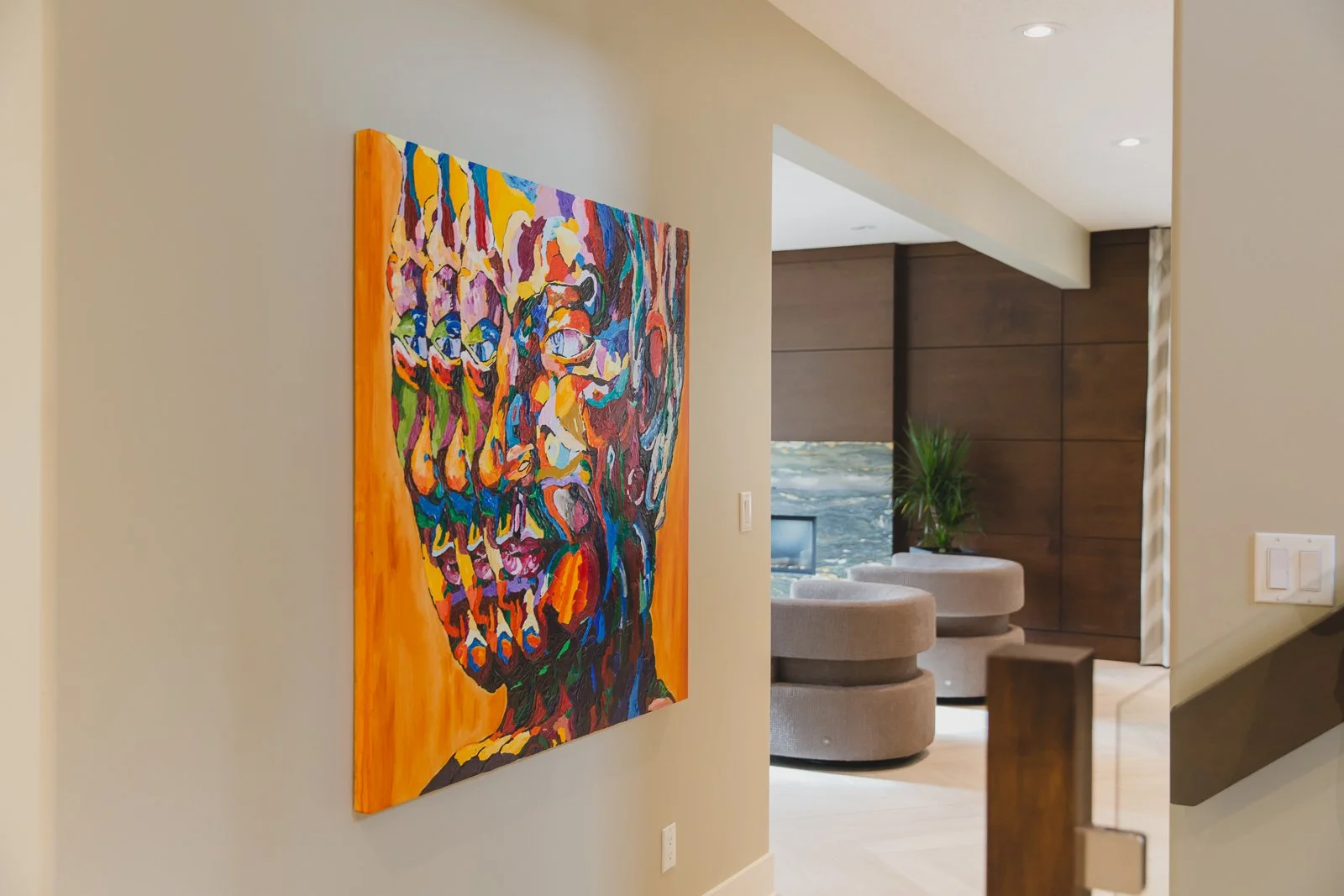 Colorful abstract painting of a human face mounted on a beige wall in a modern living room, with light wood flooring and furniture.