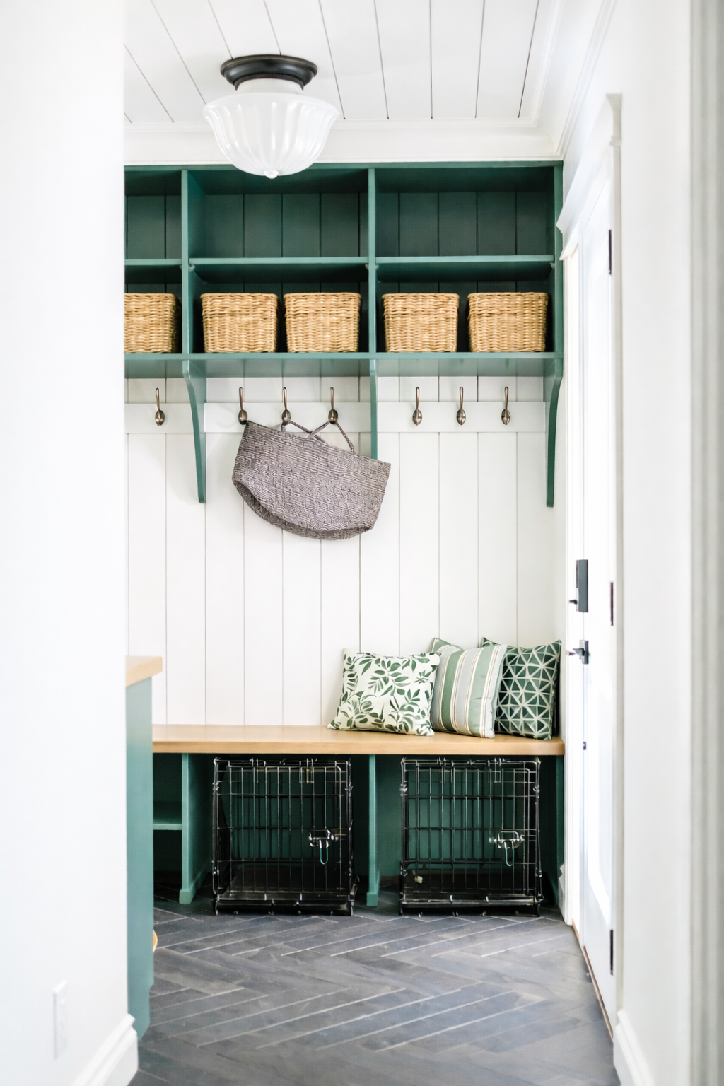 Cozy entryway with green built-in shelves, wicker baskets, hooks with bags, pillows, and wire crate pet cages.