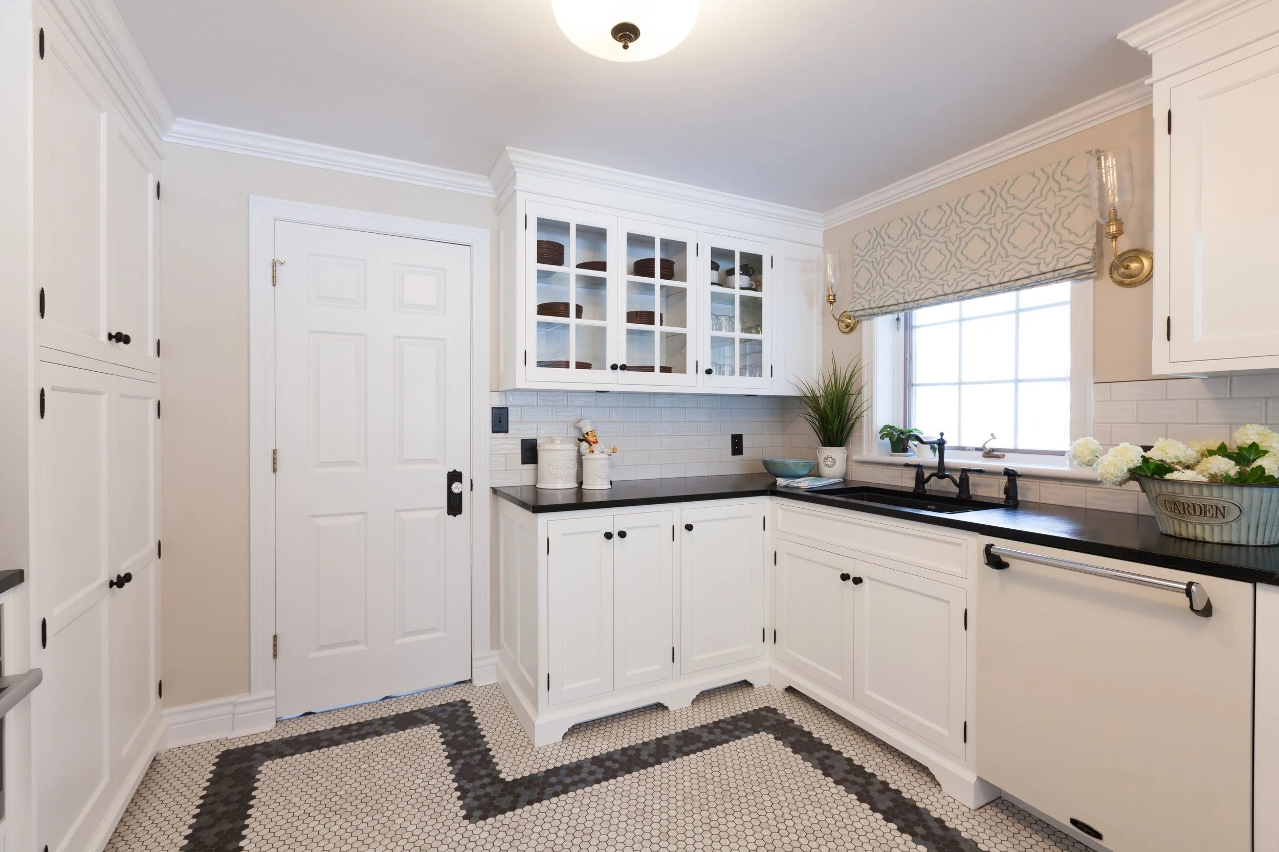 Bright kitchen with white cabinets, black countertops, a window with a patterned valance, and a plant on the windowsill.