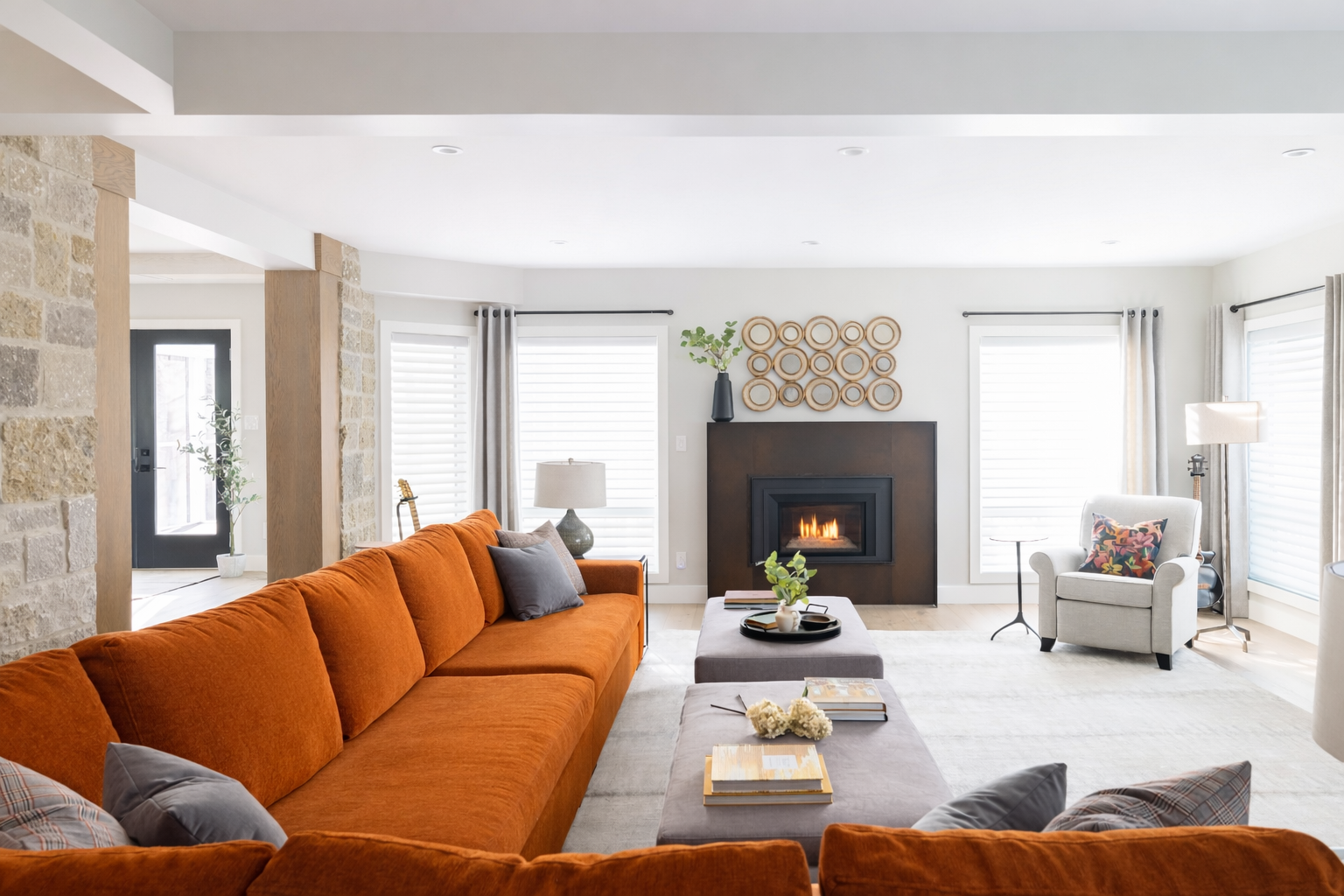 Living room with orange sofa, white armchair, fireplace, large windows with blinds, and modern decor.