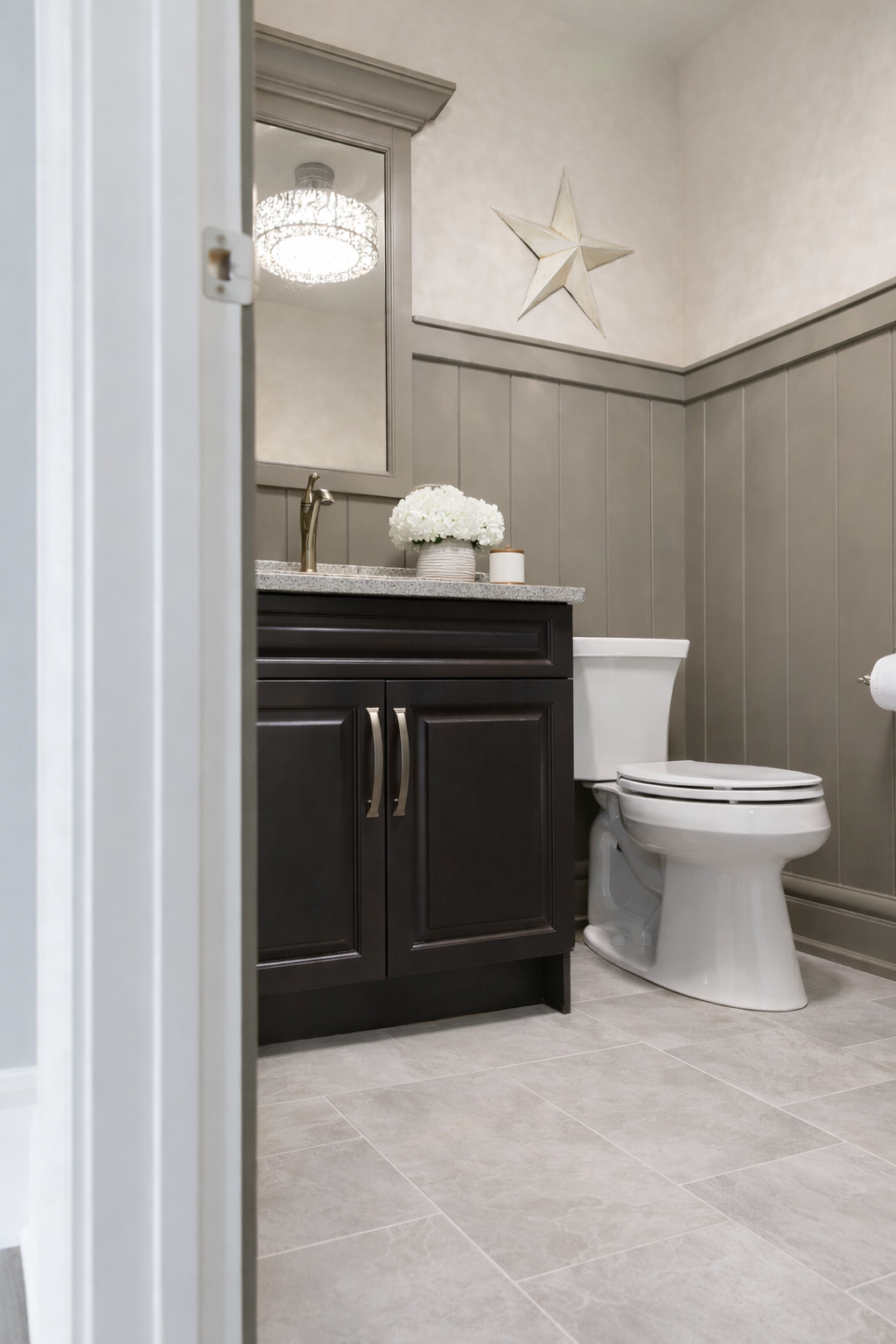 A view of a bathroom with a dark vanity, a white toilet, a granite countertop, a mirror, and a star-shaped wall decoration.