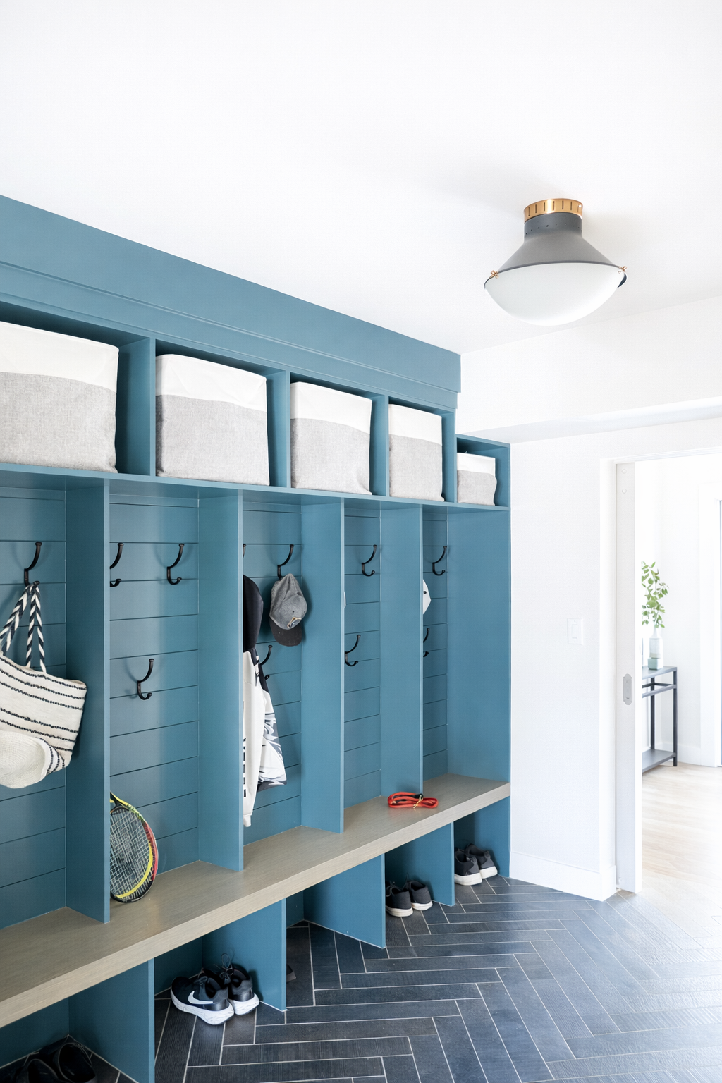 Indoor mudroom with blue cubby storage, hooks, and bins for shoes and accessories, near a white wall and ceiling light fixture.