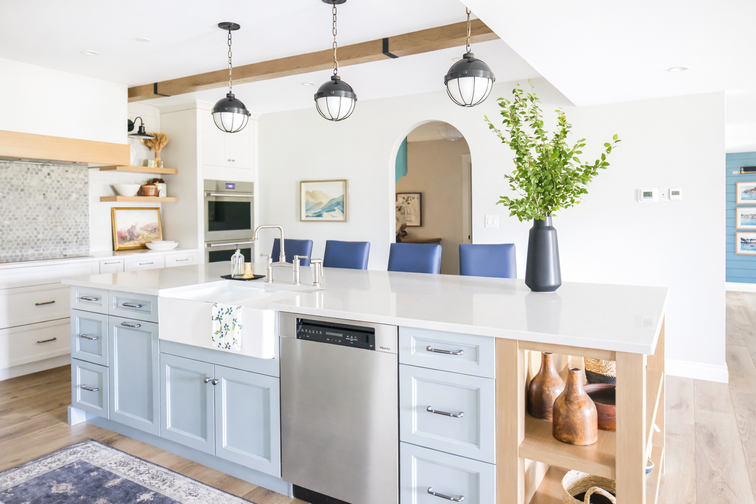 Modern kitchen with white island, blue cabinetry, and pendant lights, featuring a vase with green foliage.