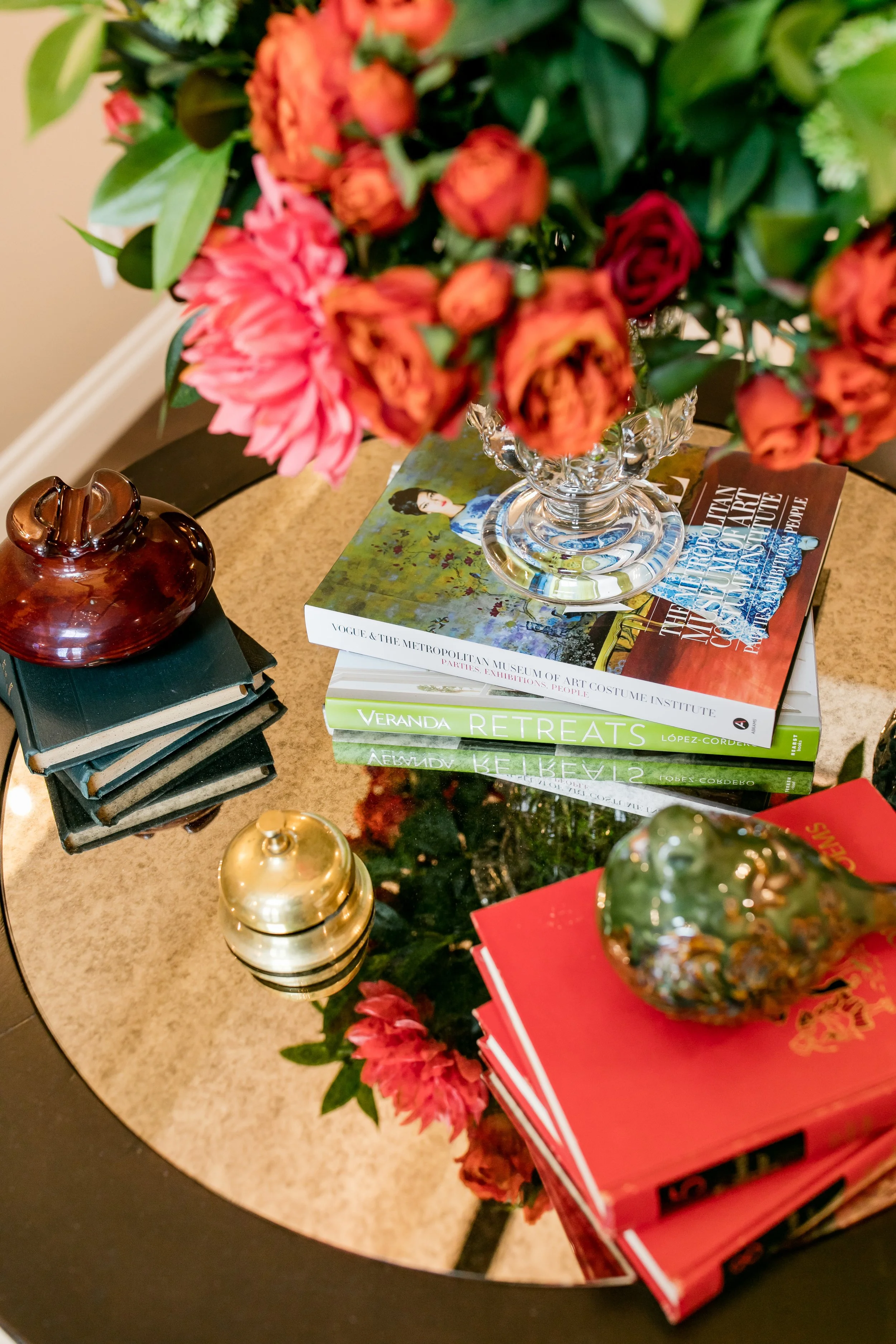 A glass vase with pink and orange flowers on top of books and decorative objects on a glass table.