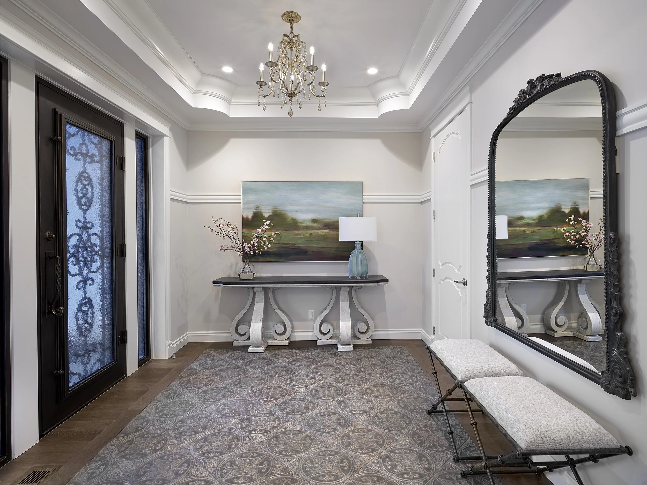 Foyer with a chandelier, a large mirror, a bench, a console table with a lamp and artwork, and a front door with decorative glass.