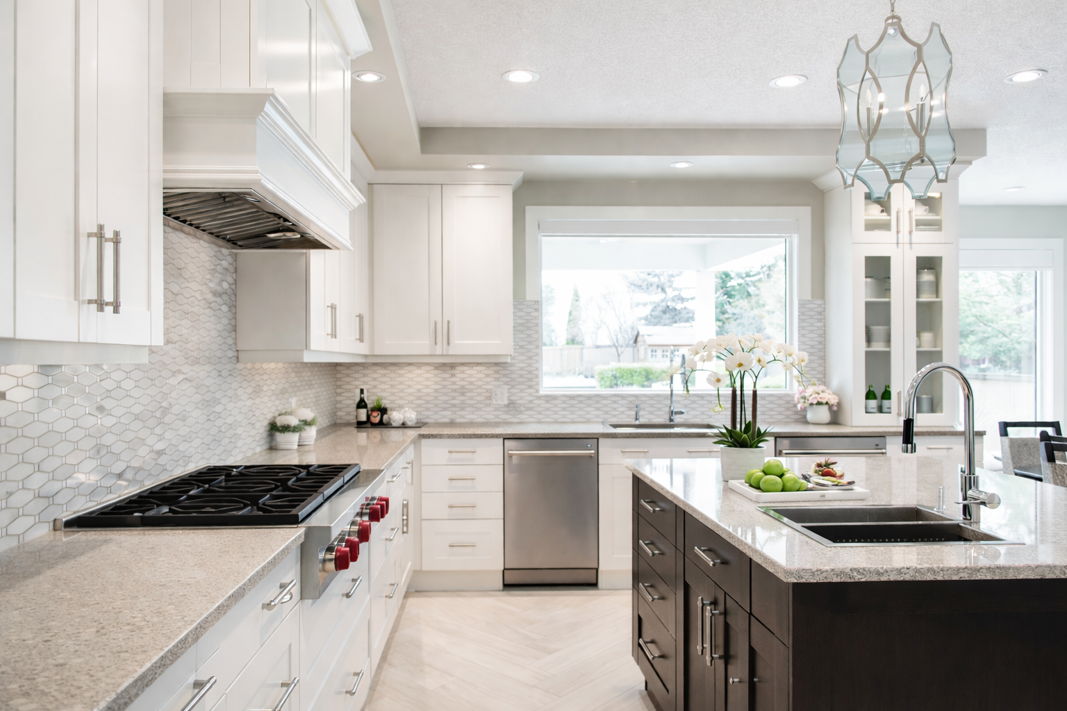 Modern kitchen with white cabinets, granite countertops, stainless steel appliances, and a central island with a sink. Decorative plants and a window overlooking the backyard.