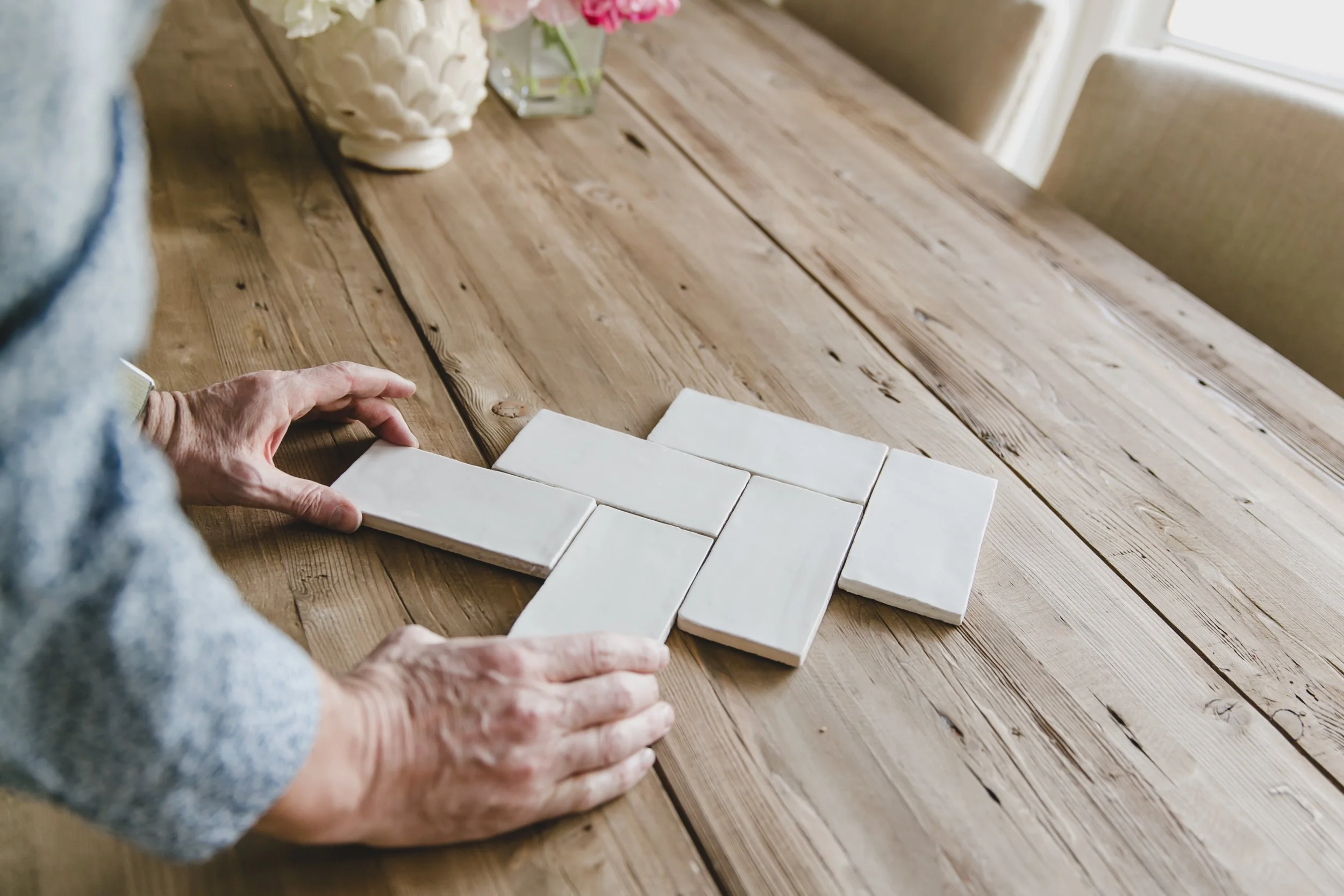 Person arranging white tiles on a wooden table to resemble a cross.