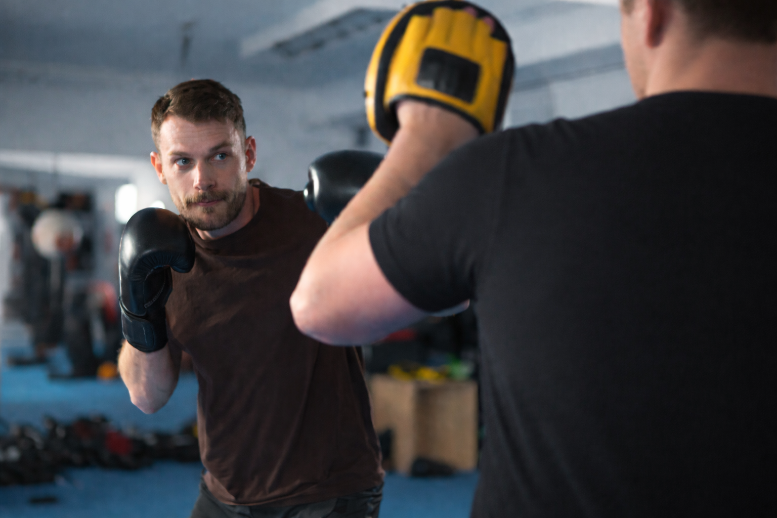 Twee personen met bokshandschoenen die een boksoefening doen in een oefenruimte.