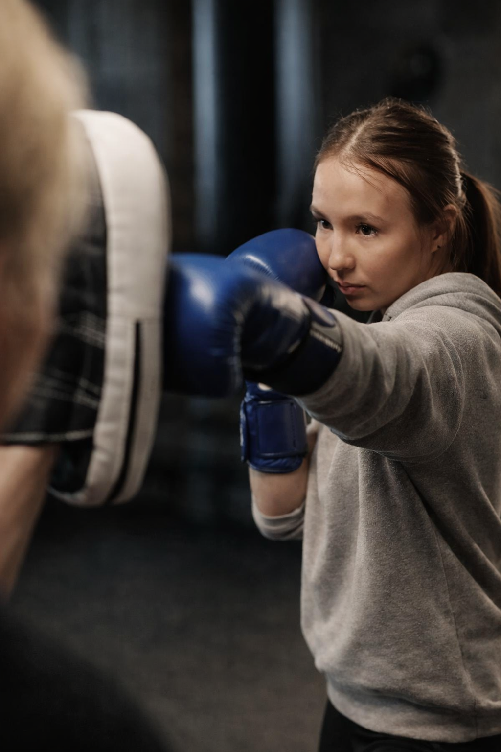 Persoon met bokshandschoenen die een stoot maakt tegen een stootkussen in een oefenruimte.