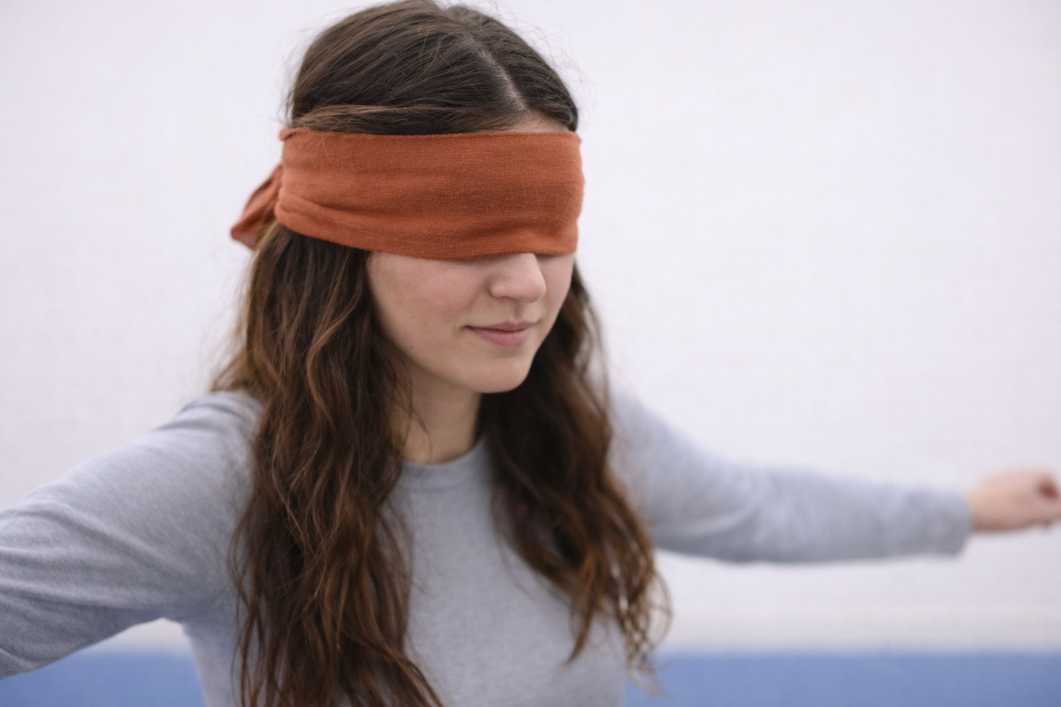 Persoon met een blinddoek voor de ogen, staand met de armen licht gespreid.