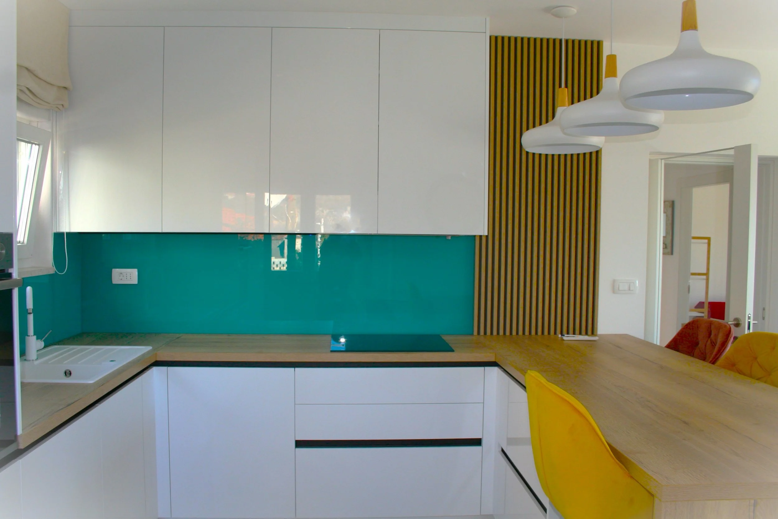Modern kitchen with white cabinets, teal backsplash, wooden countertops, and yellow chairs.