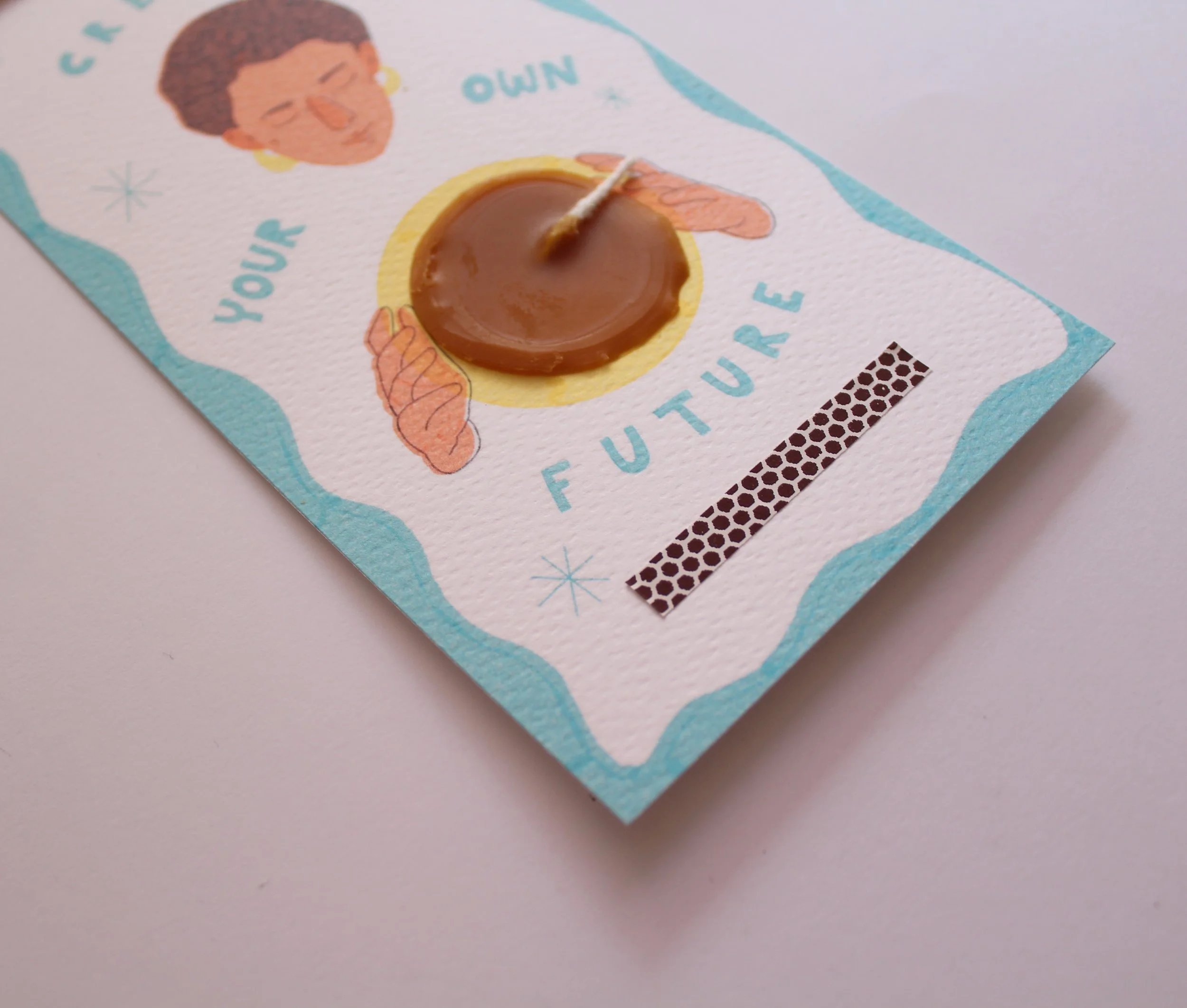 Tarjeta física con una vela de cera en el centro, decorada con ilustraciones de una mujer y la frase 'Your future' en letras azules, sobre fondo blanco con borde azul