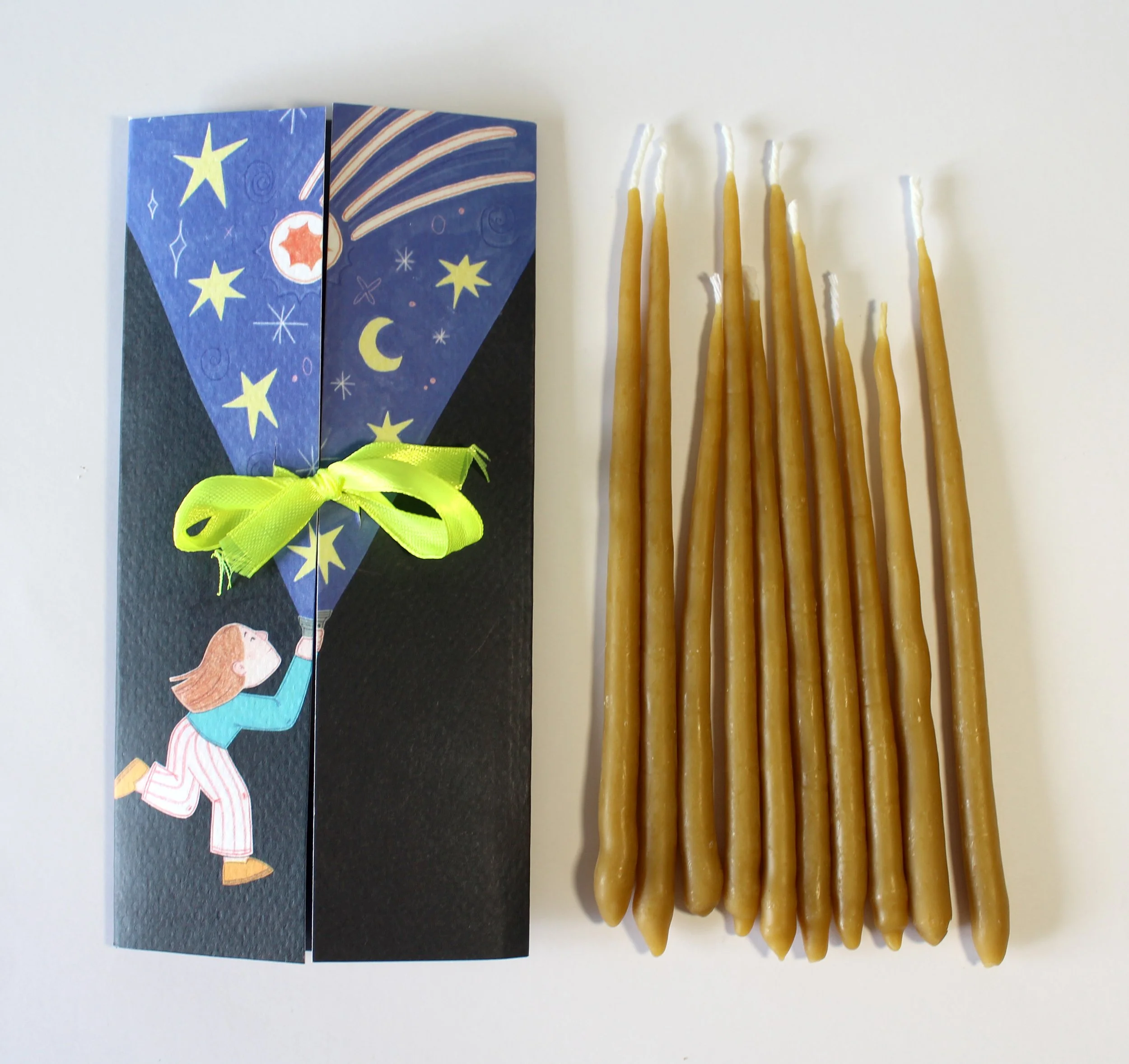 Una caja de regalo con ilustraciones de estrellas y la luna, y varias velas largas y delgadas de color marrón.