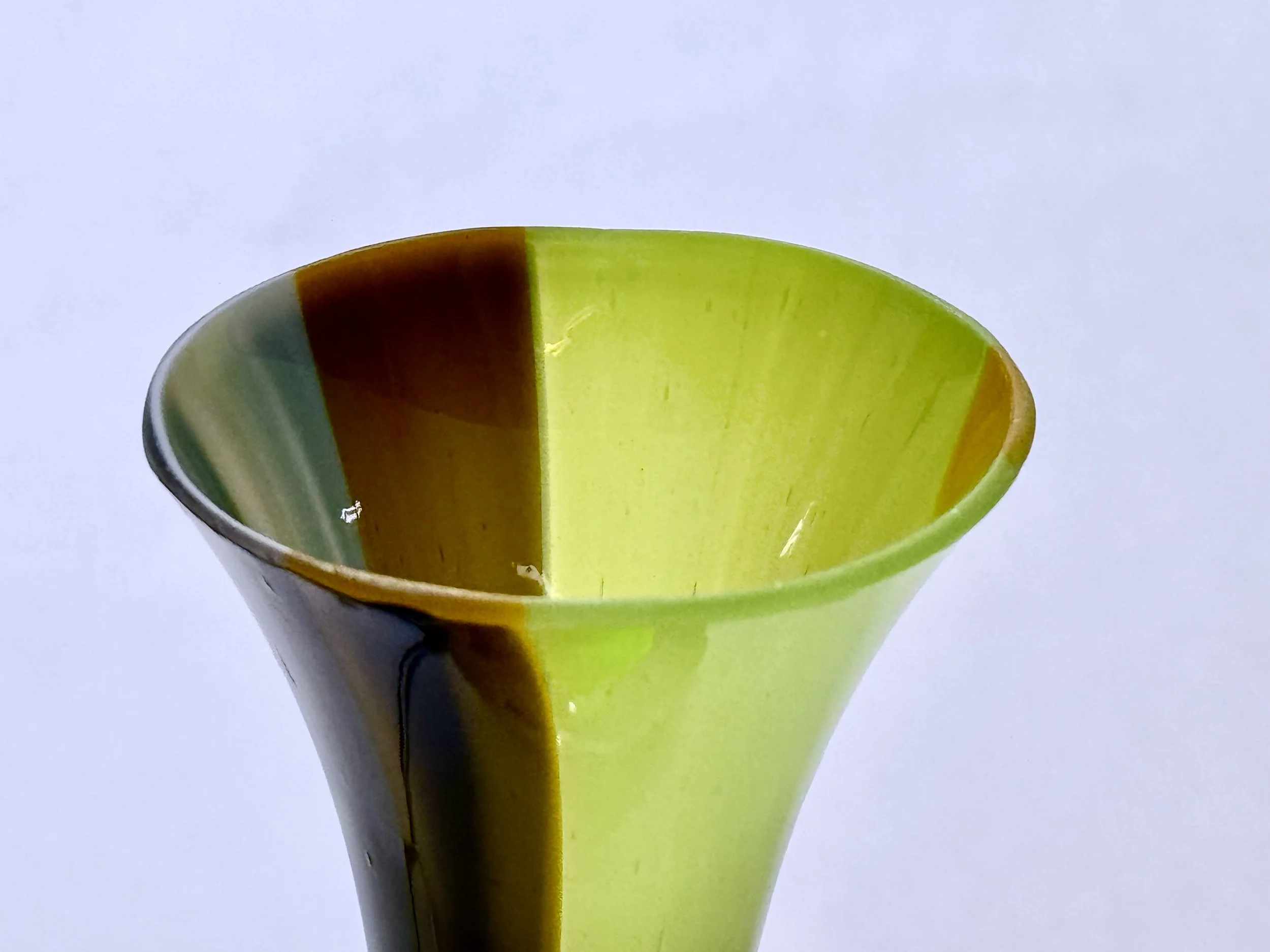 Close-up of a ceramic vase with a wide mouth, painted in vertical stripes of black, green, and yellow.