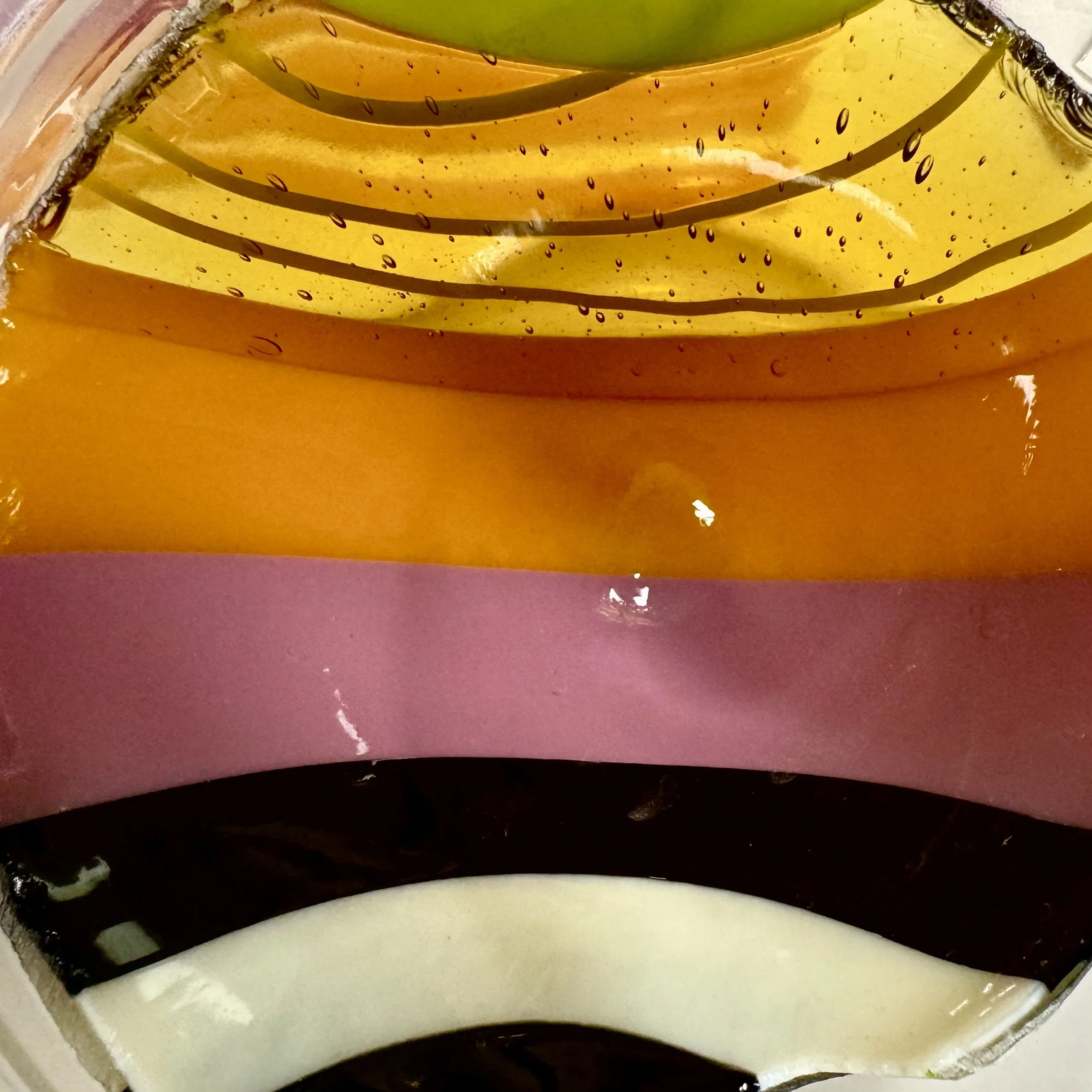 A close-up view of a palette with several horizontal stripes of oil paint in shades of pink, orange, yellow, green, brown, and white.