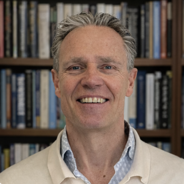 Smiling middle-aged man with gray hair in front of bookshelves.