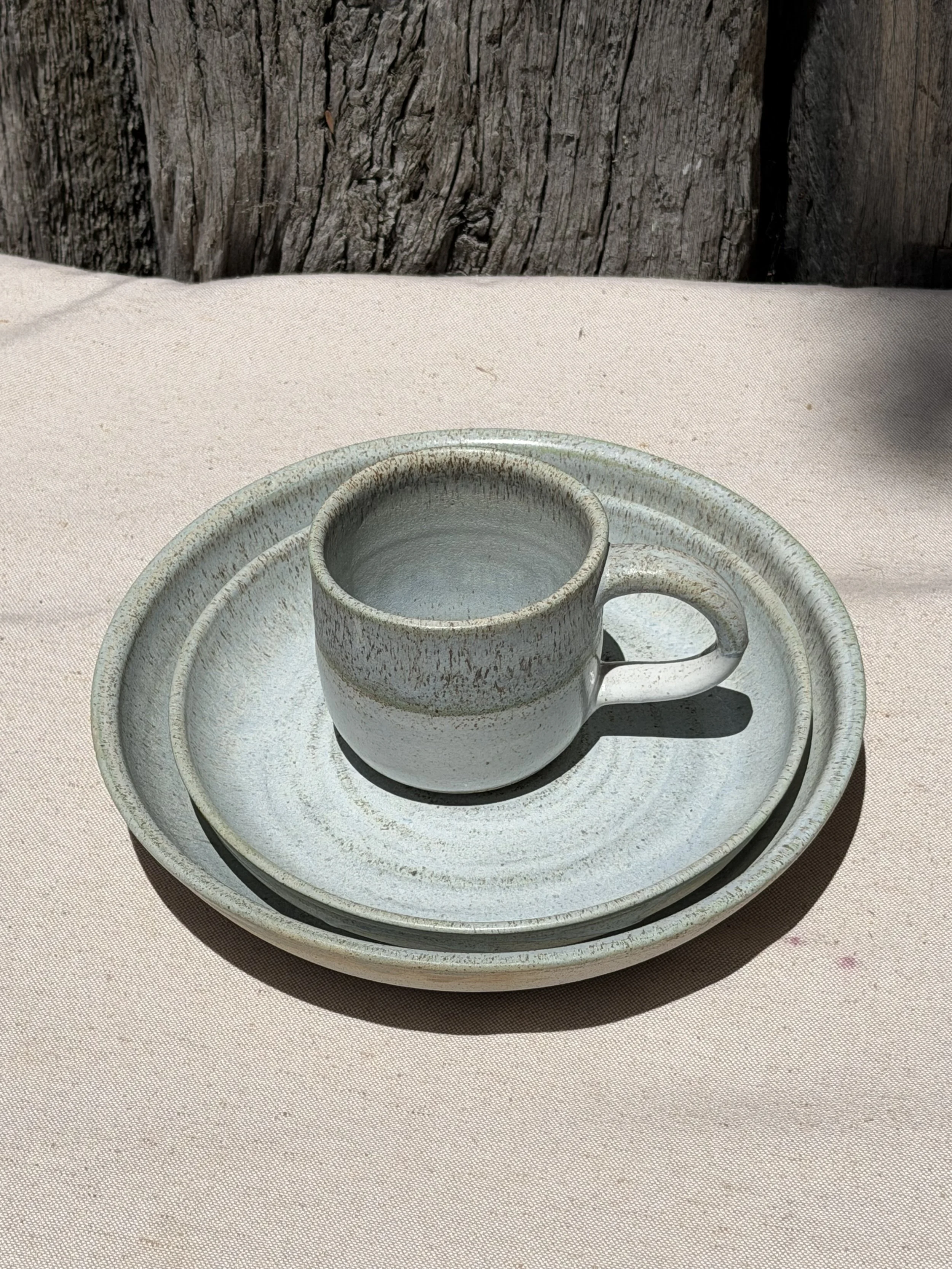 A ceramic cup on a matching saucer and plate, placed on a pink cloth surface with a wooden background.
