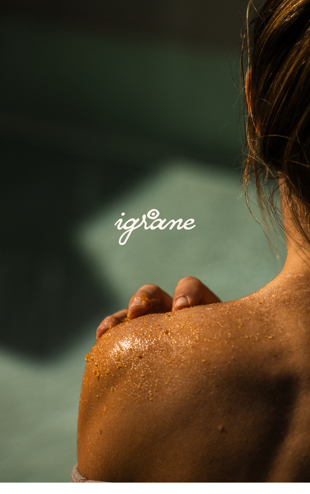 Une personne appliquant un gommage corporel sur son épaule, avec une texture granuleuse et dorée, sous une lumière douce.