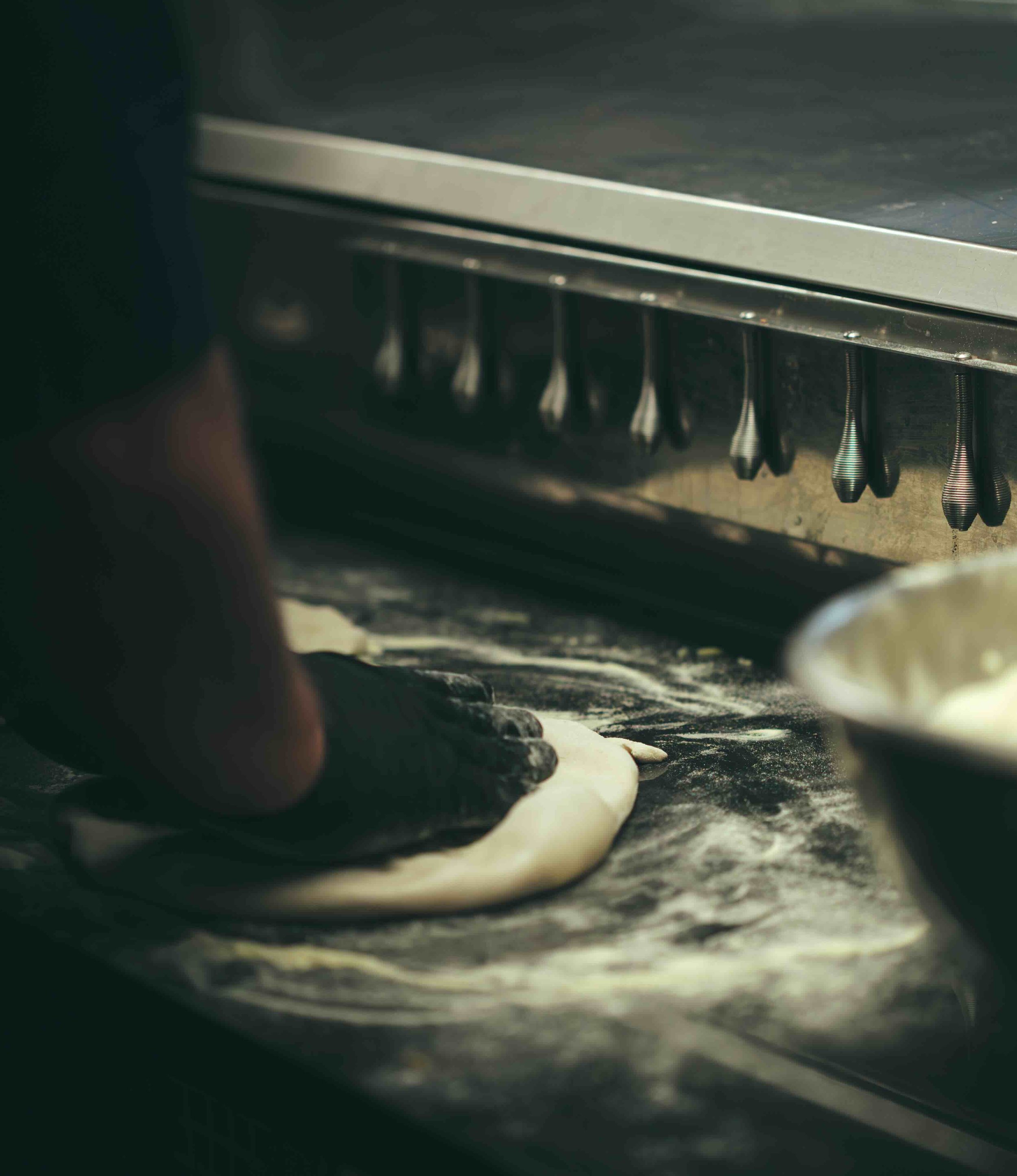 Personnes en train de façonner une pâte à pizza sur une surface farinée, sous une plaque de cuisson