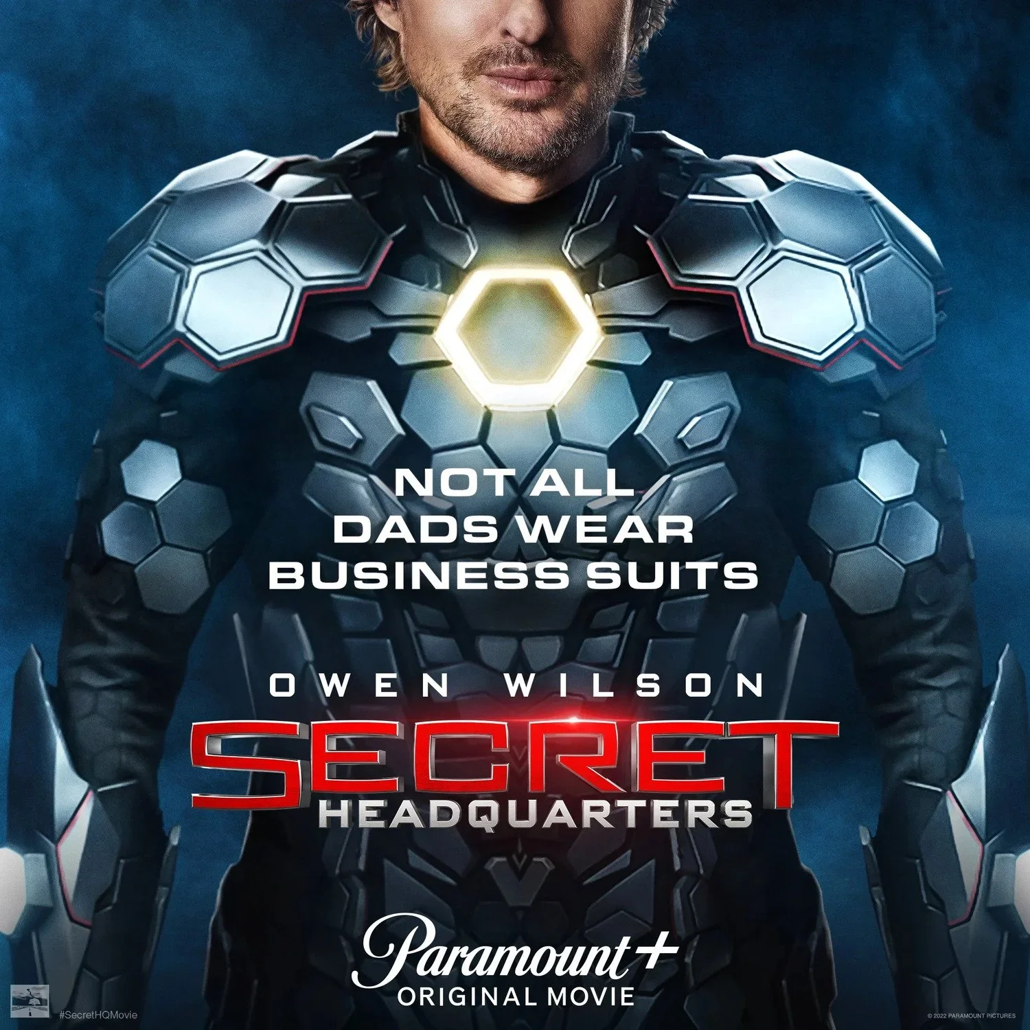 A digitally created image of a man in a futuristic armor suit with hexagonal patterns and glowing accents. The suit has a central glowing hexagon on the chest. Overlaid text reads, 'Not all dads wear business suits', 'Owen Wilson', 'Secret Headquarte