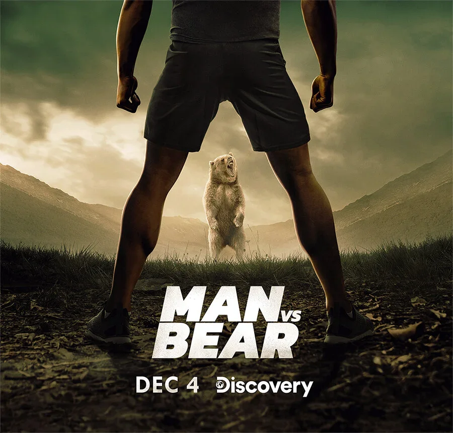 A man standing with legs apart, viewed from behind, with a bear in the background standing on its hind legs in a mountain landscape. Text indicates the show 'Man vs Bear' airing on December 4 on Discovery.