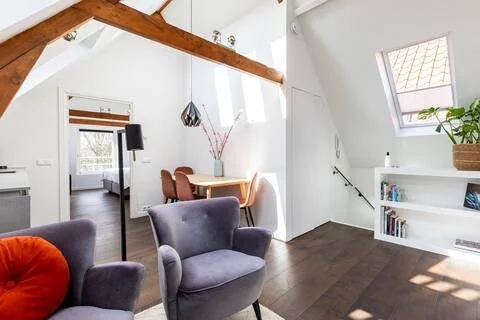 Living room with a dining area, purple armchair, wooden ceiling beams, and a window with a view.