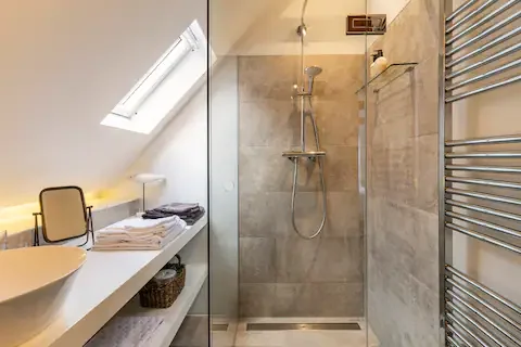 Modern bathroom with a walk-in shower, tiled walls, a heated towel rack, a sink on a white countertop, and a sloped skylight in the ceiling.