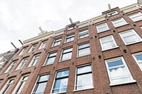 A tall, multi-story brick building with several windows and visible sky.