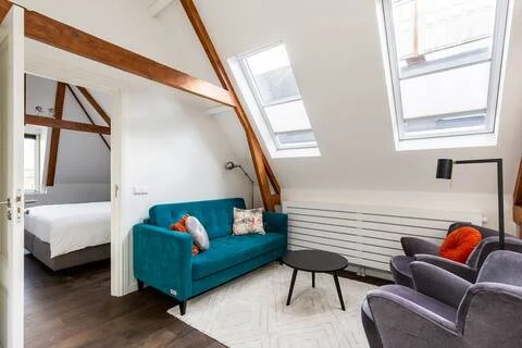 Living room with a blue sofa, gray armchairs, black coffee table, and skylight windows in an attic space.