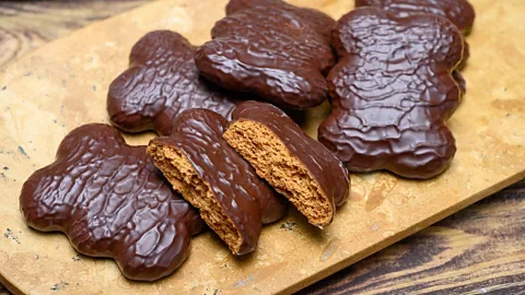 Chocolate-covered cookies on a wooden surface, with one broken in half to show the inside.