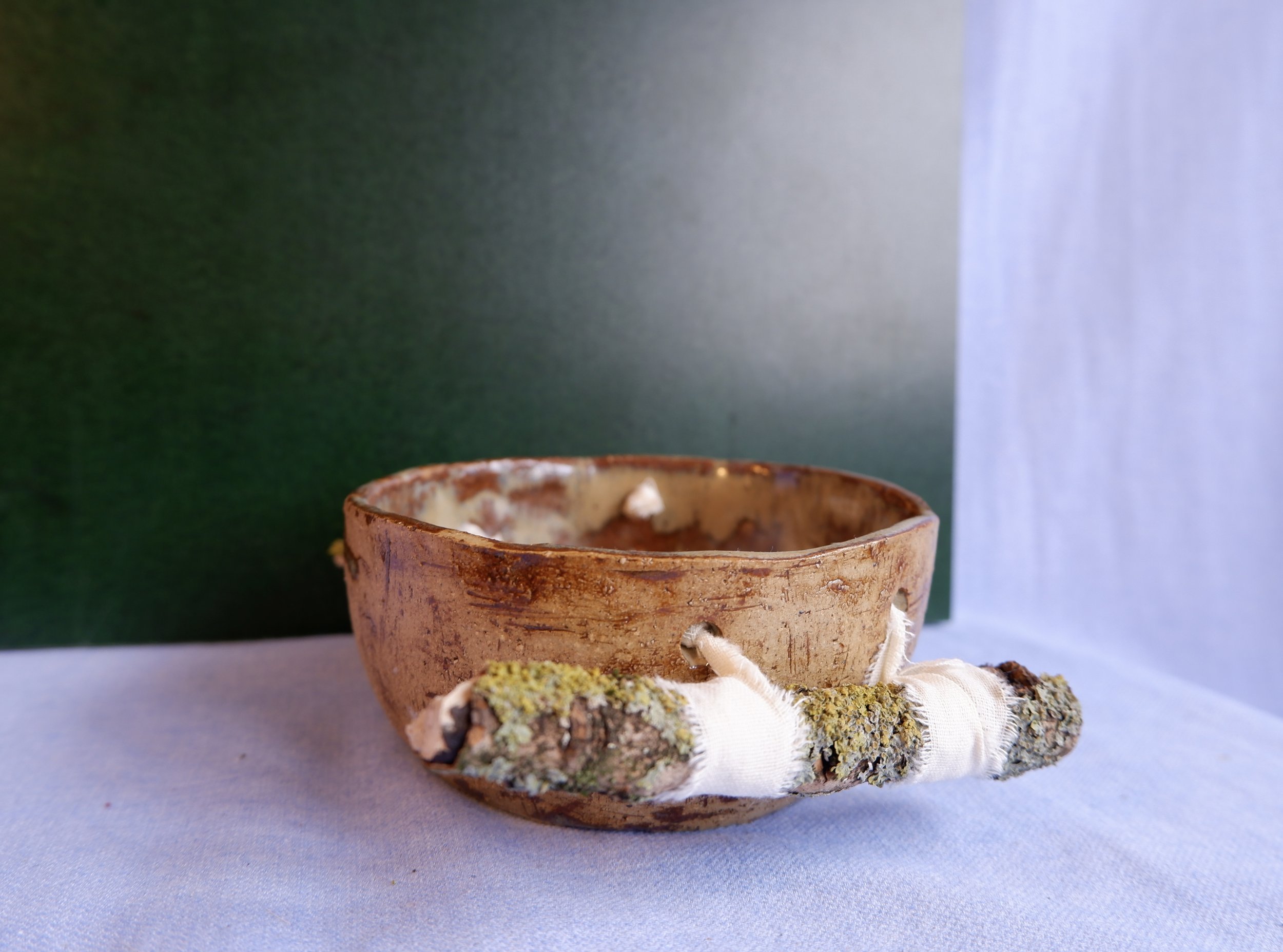Bowl made from yellow clay, bound to two branches.