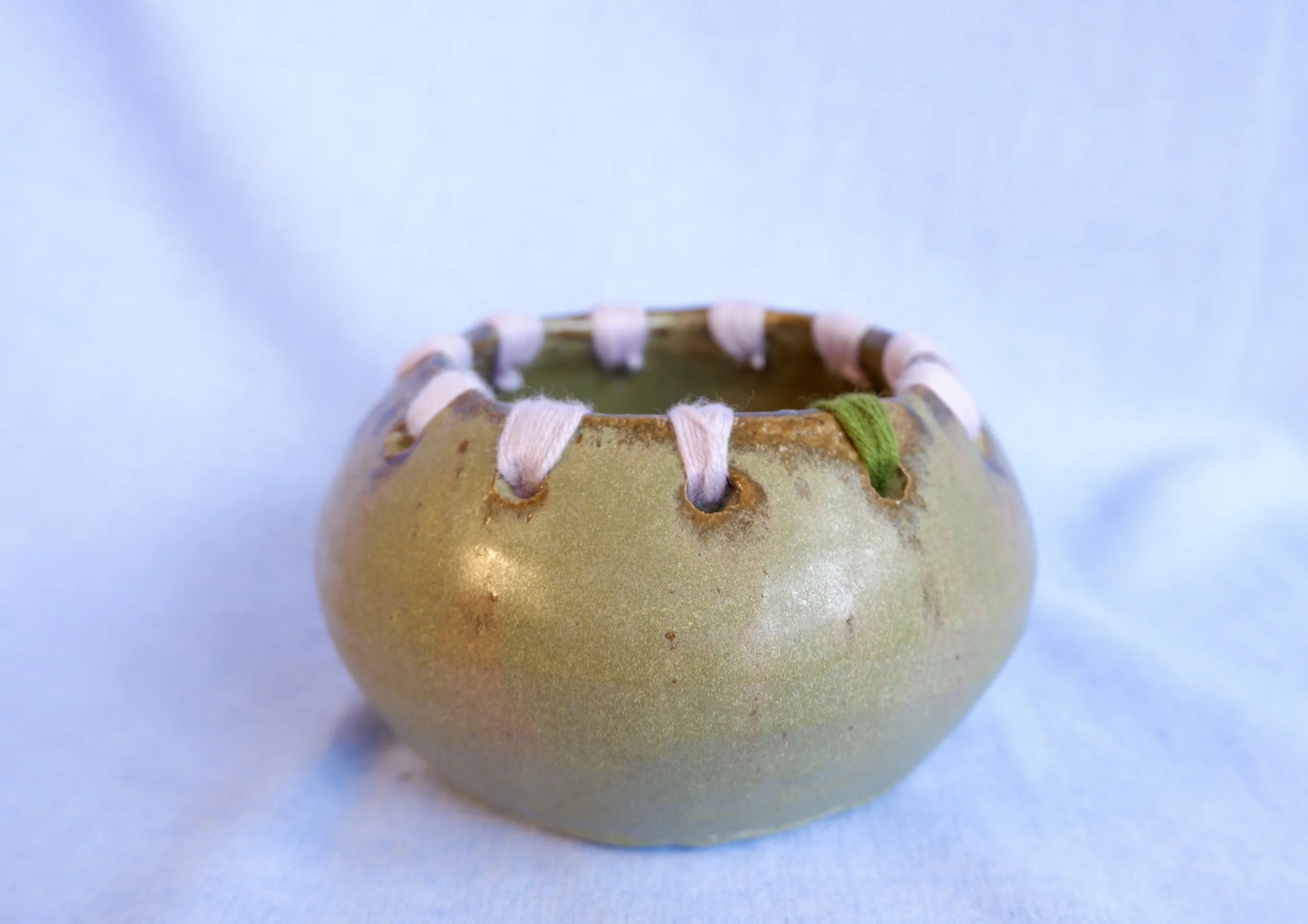 Moss-green ceramic bowl with wool-thread detailing.