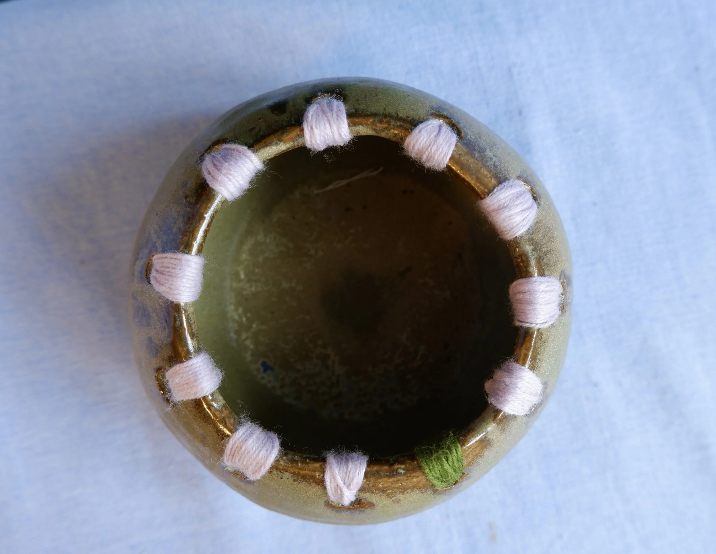 Moss-green ceramic bowl with wool-thread detailing.