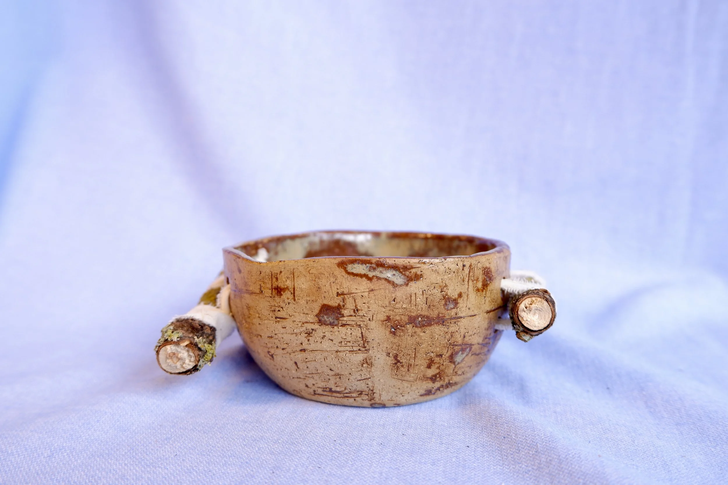 Bowl made from yellow clay, bound to two branches.