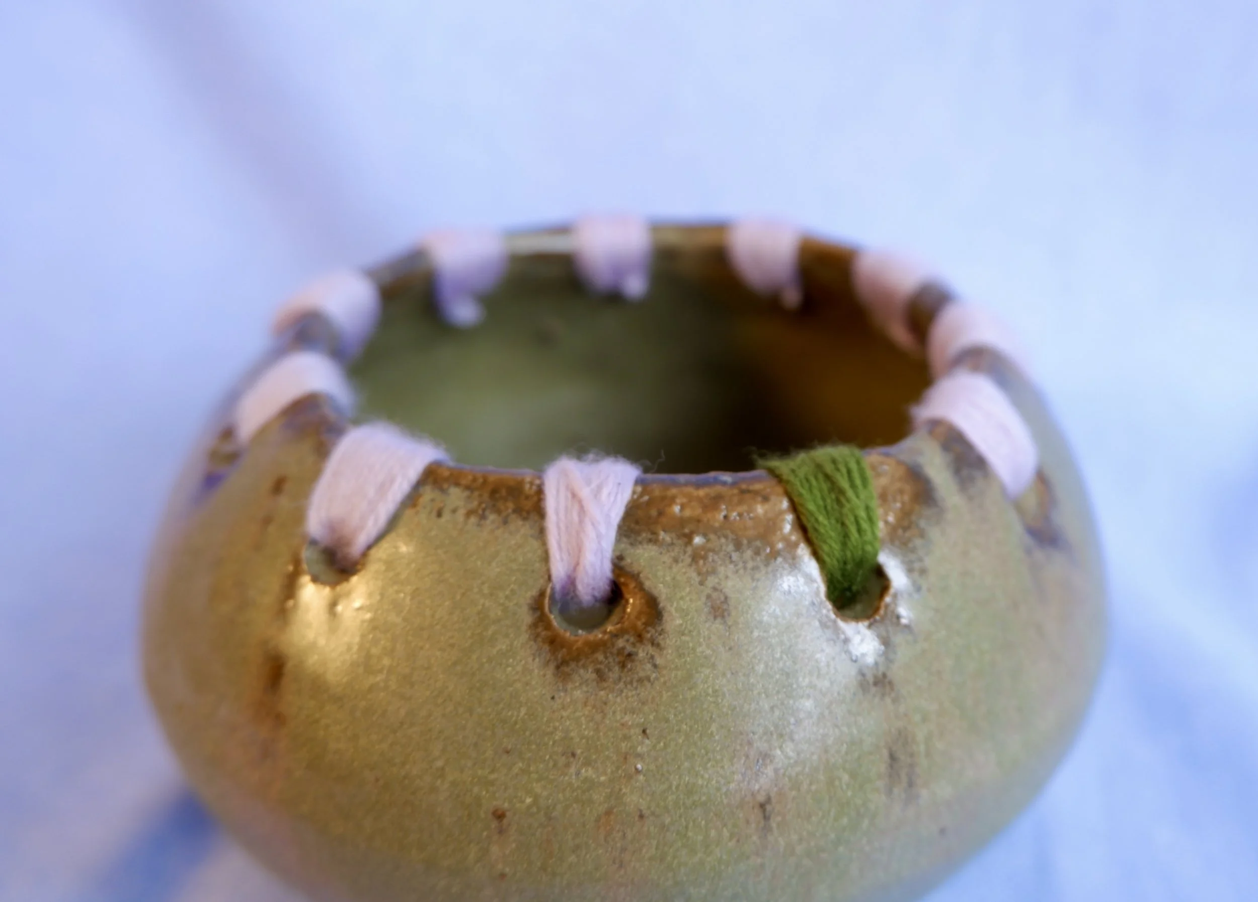 Moss-green ceramic bowl with wool-thread detailing.