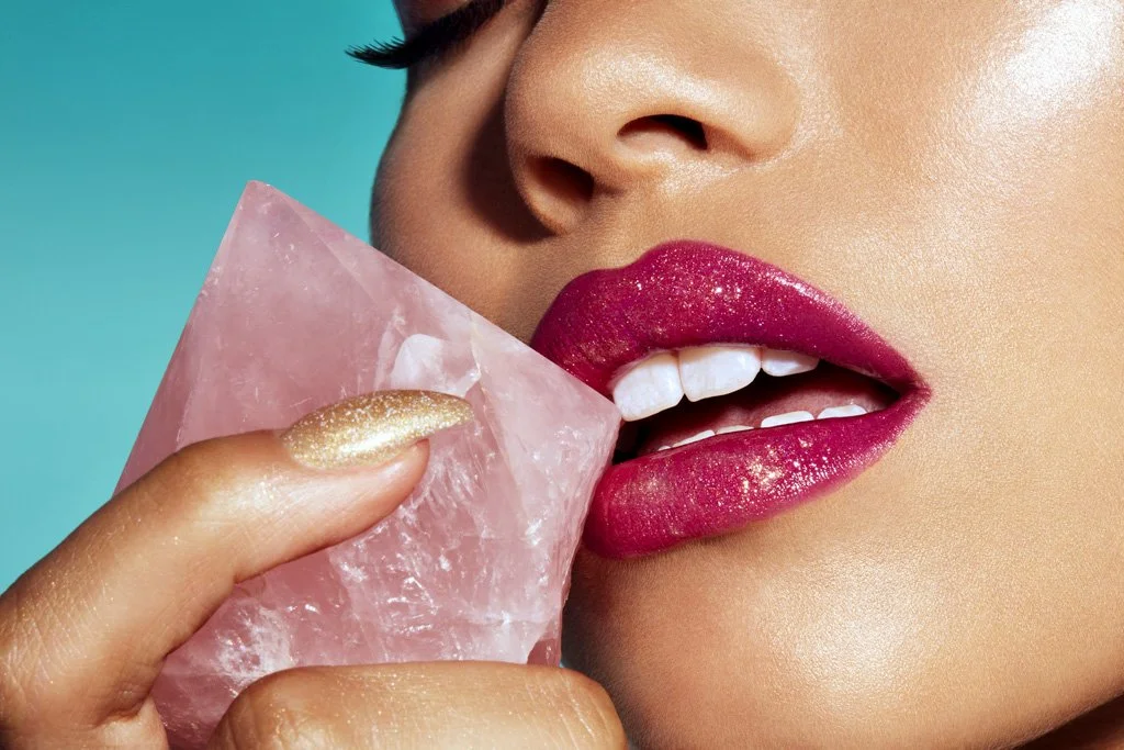A woman with glossy pink lipstick biting a large pink stone