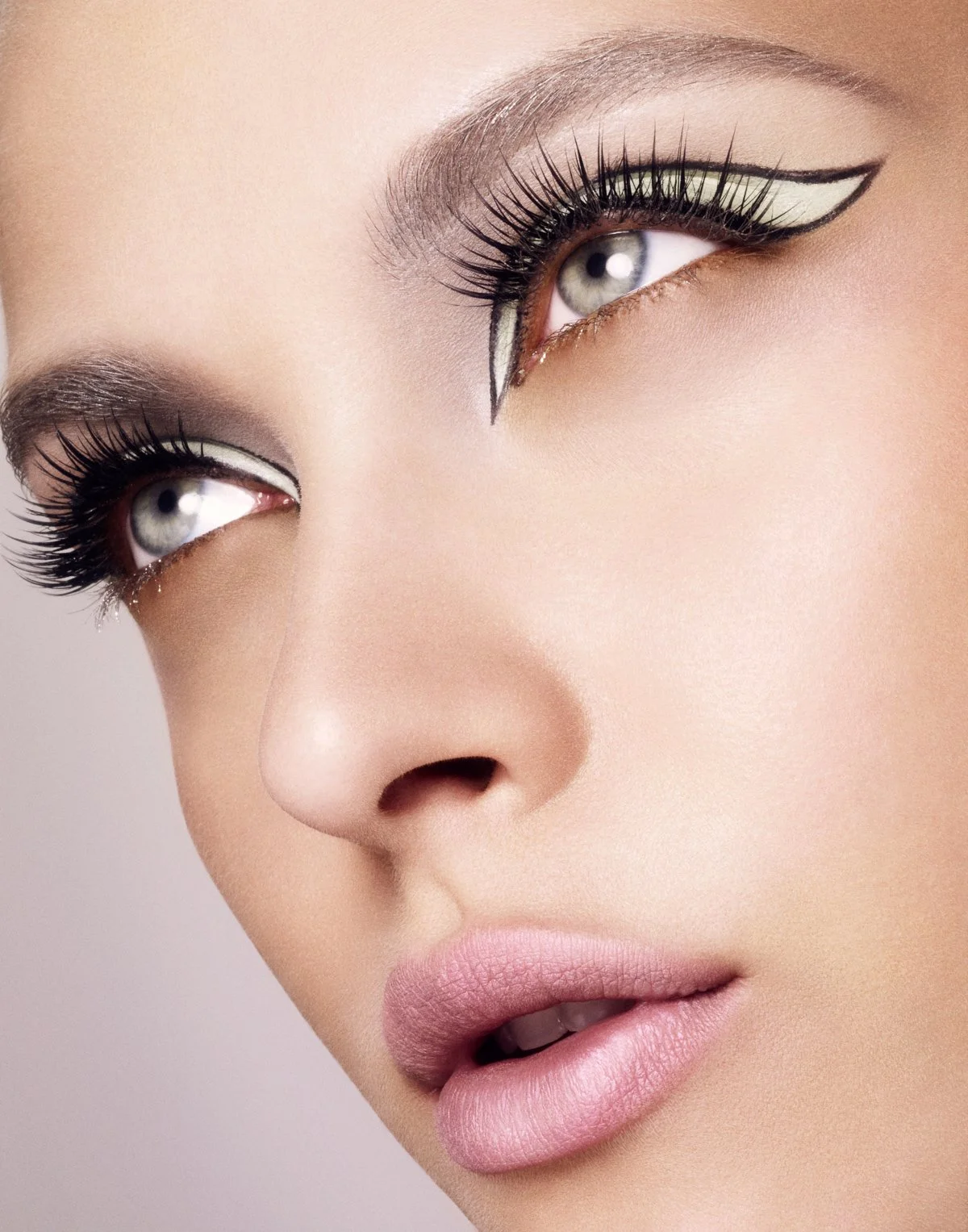 Close-up of a woman's face focusing on her eyes and lips with bold makeup, including cat-eye eyeliner and voluminous lashes.