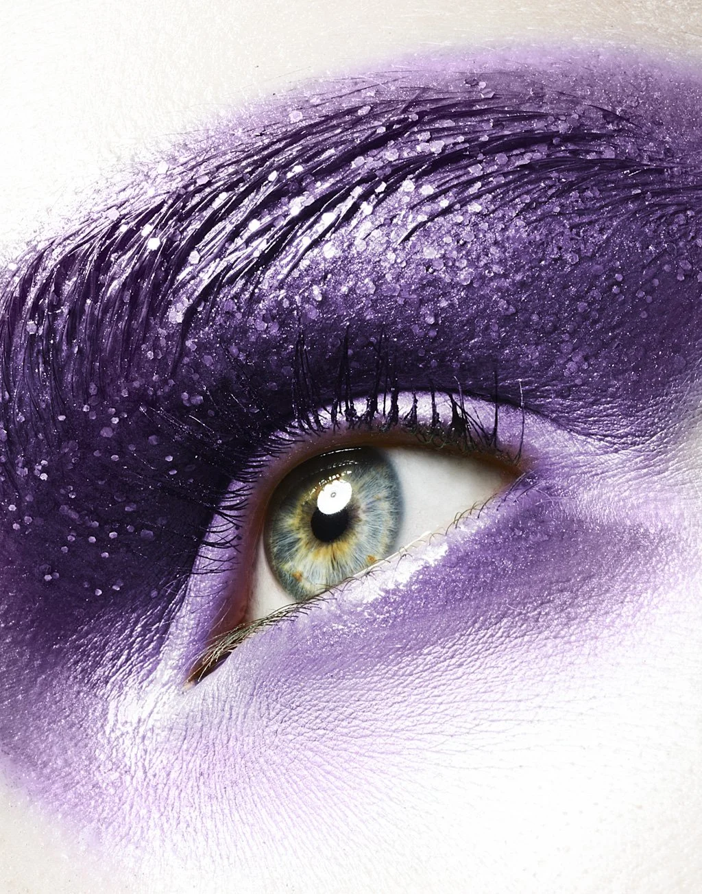 Close-up of a human eye with purple eyeshadow and glitter, showing the iris and eyelashes.