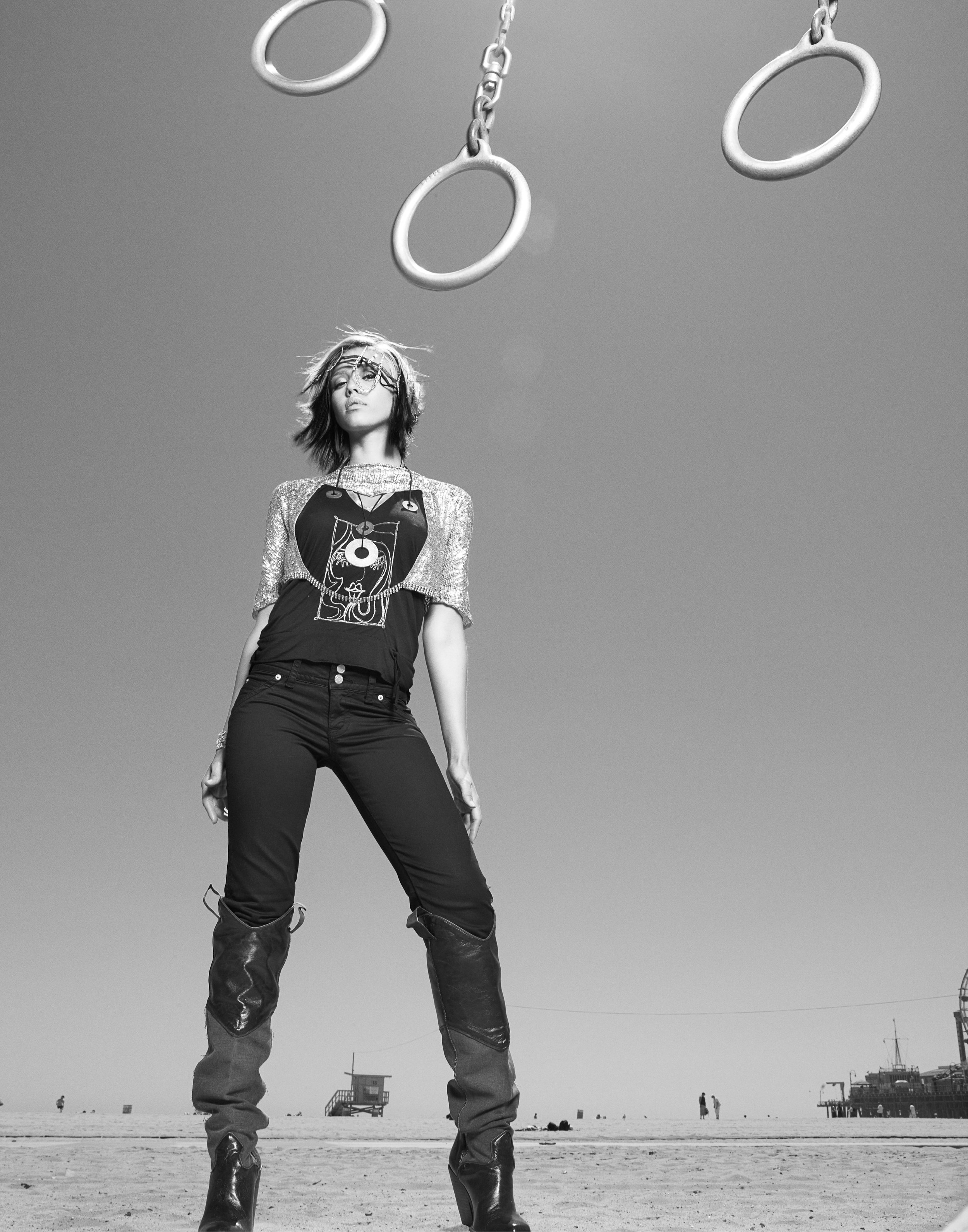 JESSICA ALBA standing on a beach with gymnastic rings hanging above her head in the sky, black and white photo.