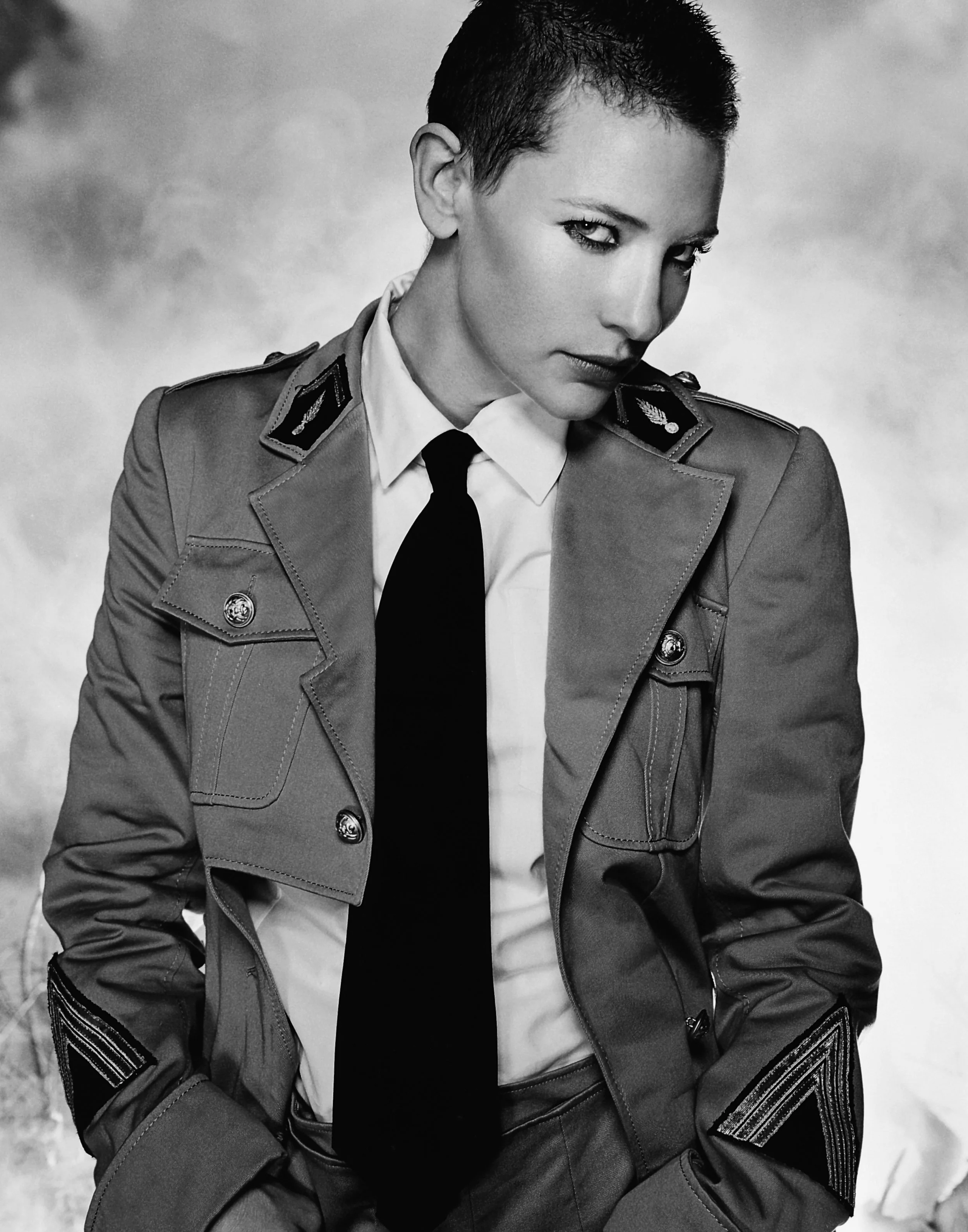 A black and white photo of CATE BLANCHETT in a military uniform with a short haircut, looking at the camera with a serious expression.