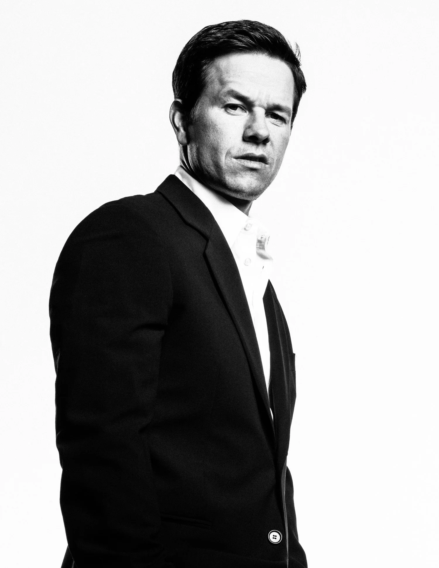 Black and white portrait of MARK WAHLBERG in a suit, looking at the camera with a serious expression, against a plain white background.